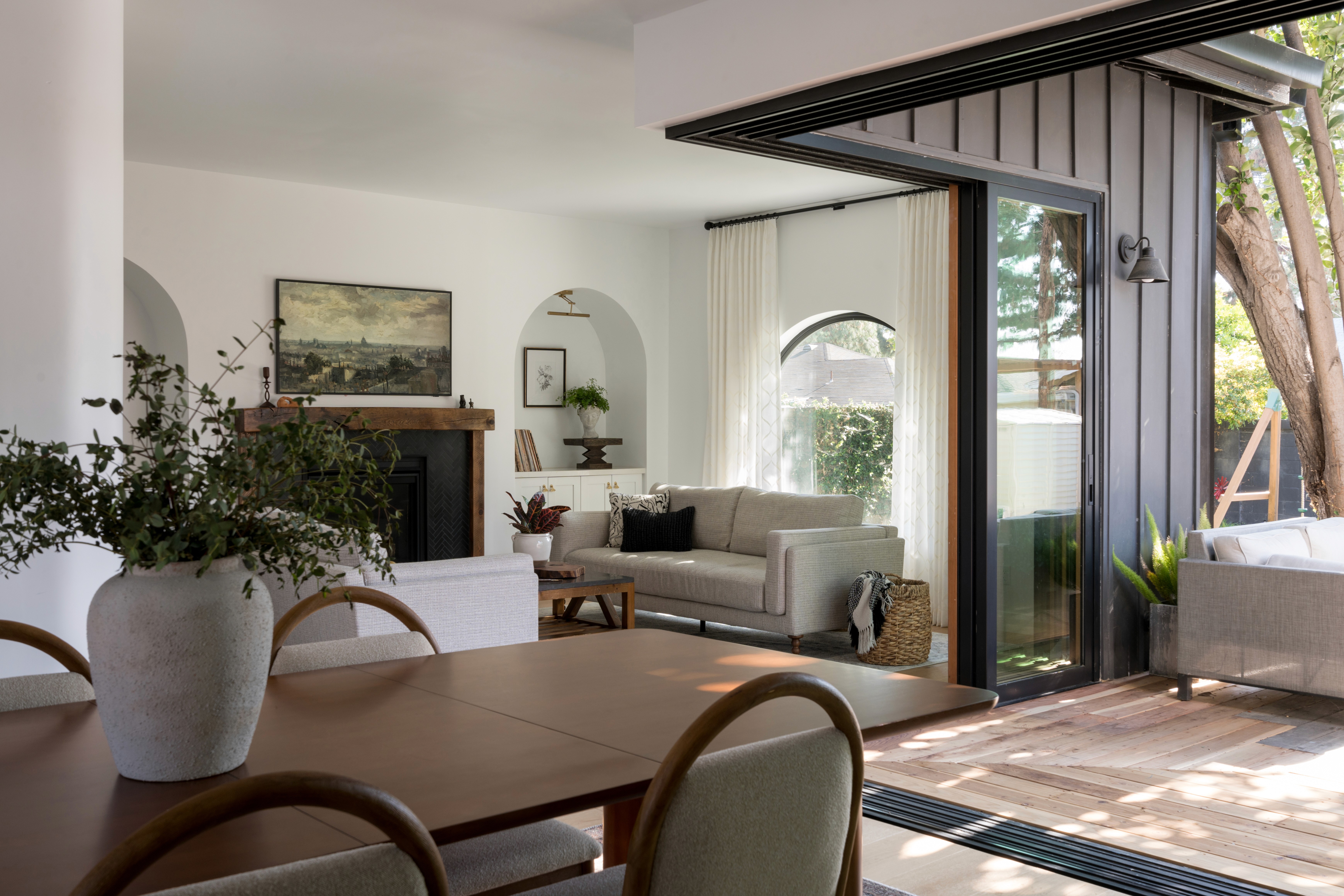 A cozy, open-concept dining and living room with neutral-toned furniture, modern fixtures, and large bi-fold doors, that allow natural light to fill the space  by Jubilee Interiors in Lakewood, California