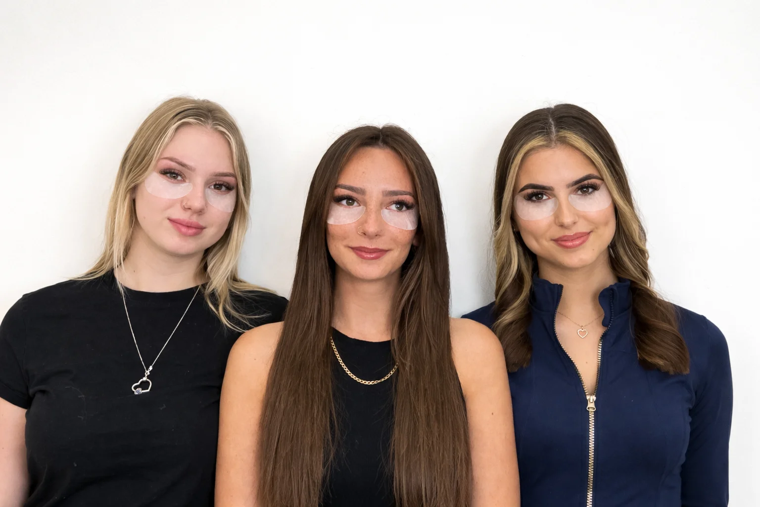 Three girls standing next to eachother showing their lash extensions and eye masks