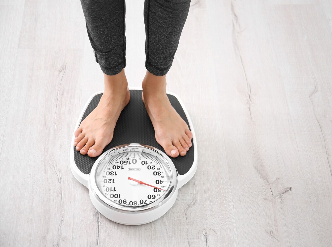 woman checking her progress on a scale at home after using an exercise bike for weight loss