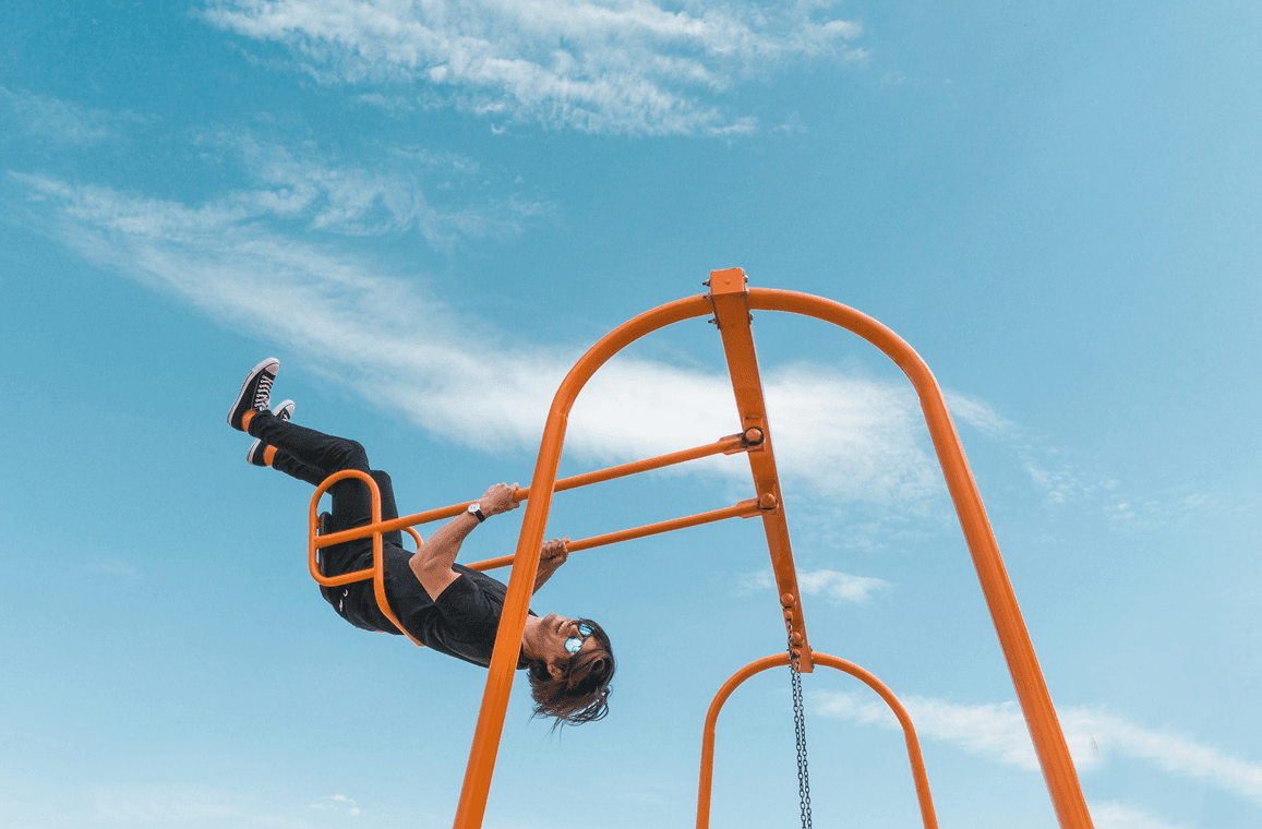 Person hanging upside down from orange playground bars against a bright blue sky.