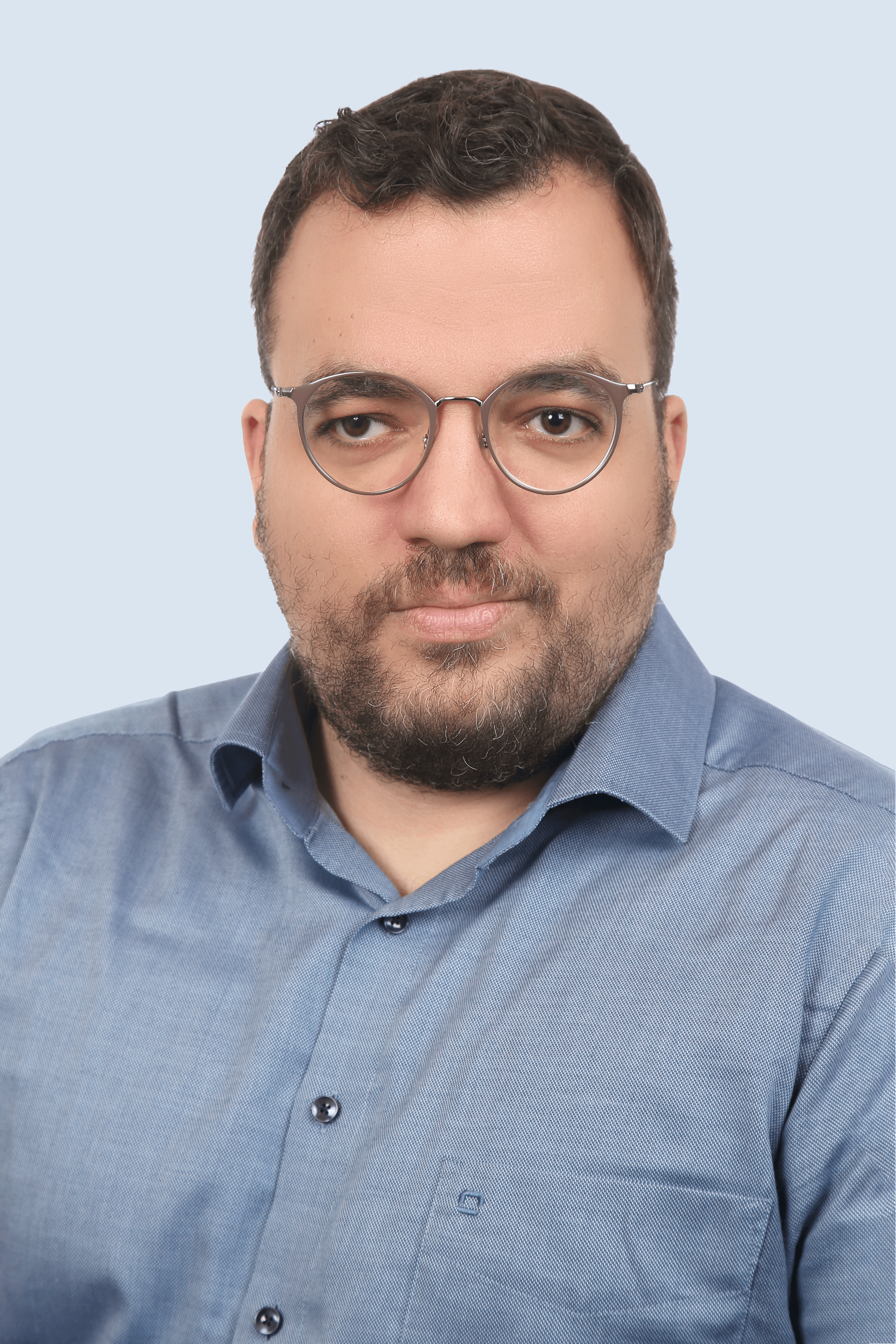 Frau mit braunem Anzug, blauem Hemd und Brille schaut mit verschränkten Armen seitlich in die Kamera und lächelt.