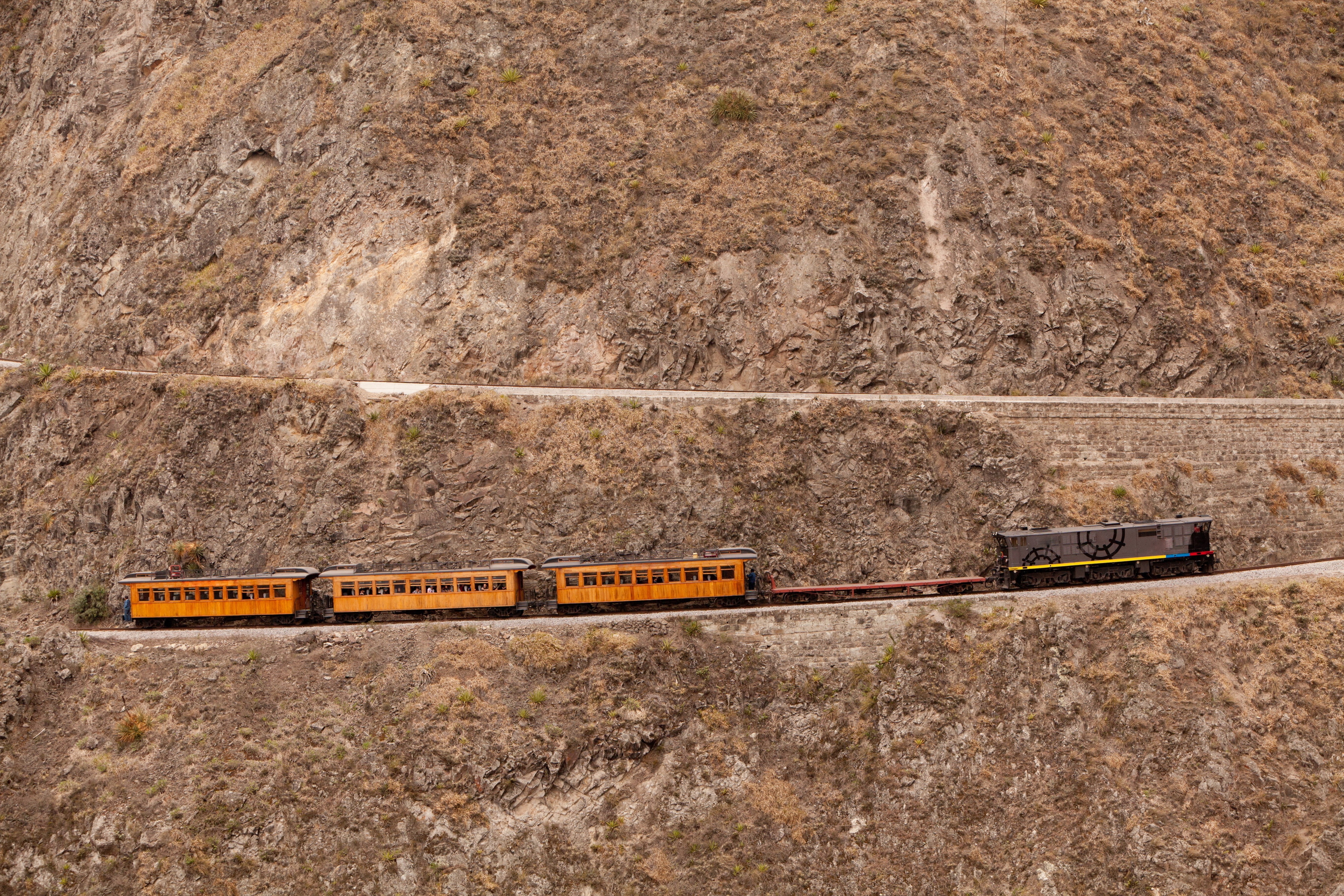 A train switchbacks up a steep, rocky ciff in the Ecuatorian Andes.