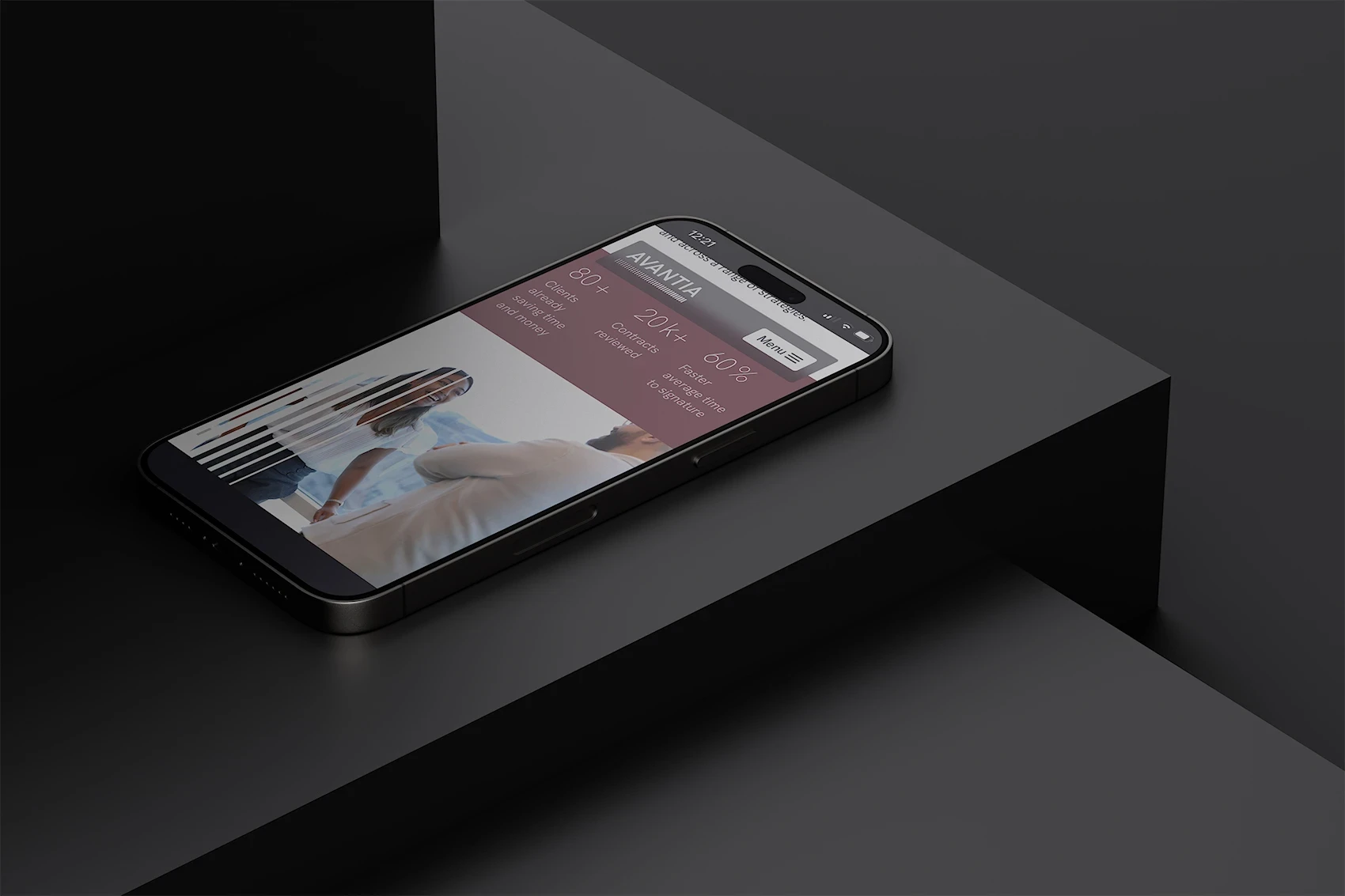 Smartphone lying on a dark surface, displaying the Avantia mobile site. The screen shows key metrics such as ‘80+ clients’, ‘20k+ contracts reviewed’, and ‘60% faster time to signature’, along with a photo of two professionals in conversation. The interface has a sleek layout with rose and white tones.
