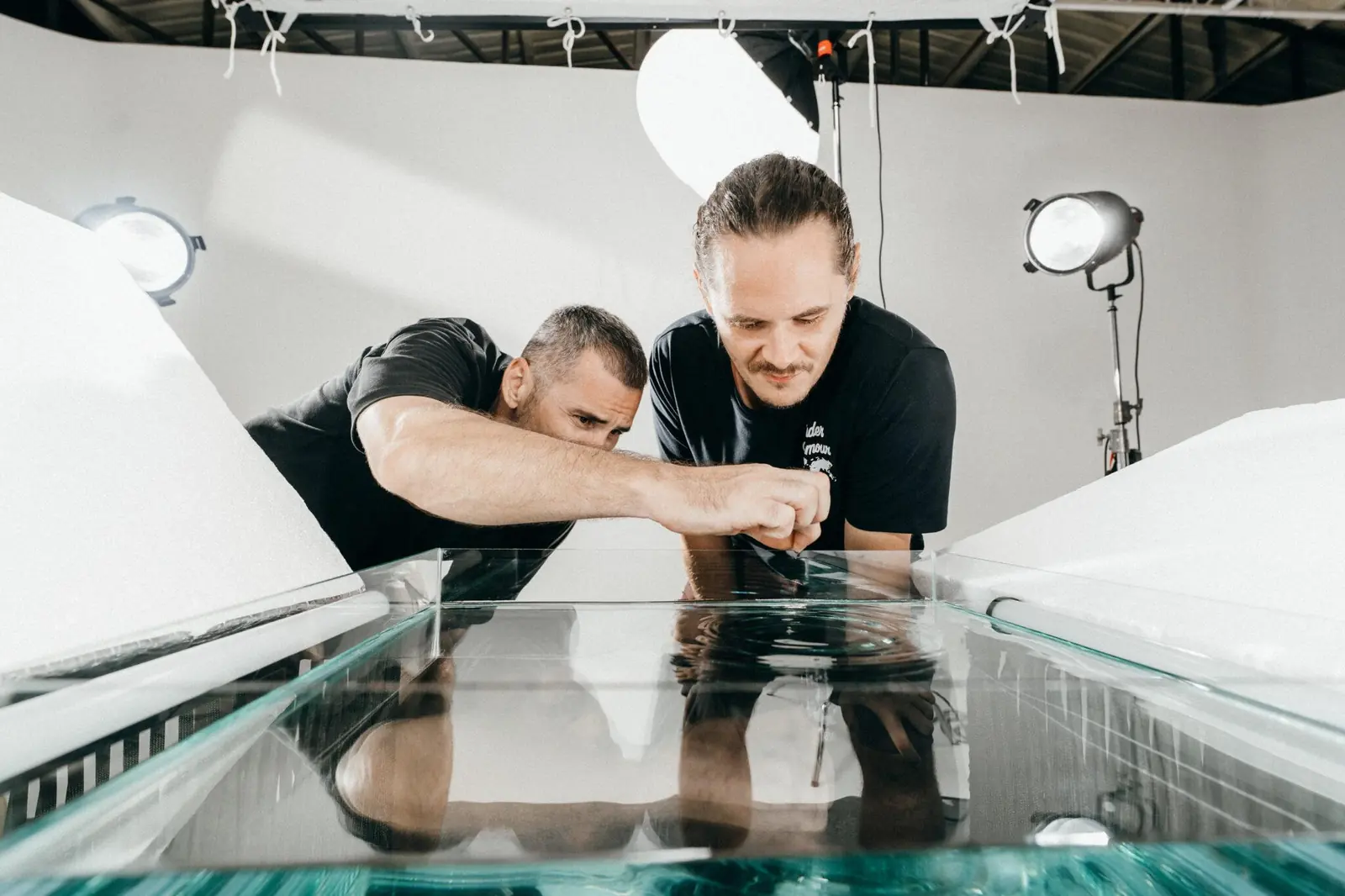 Two crew members setting up a glass water tank for product shots on the white cyclorama