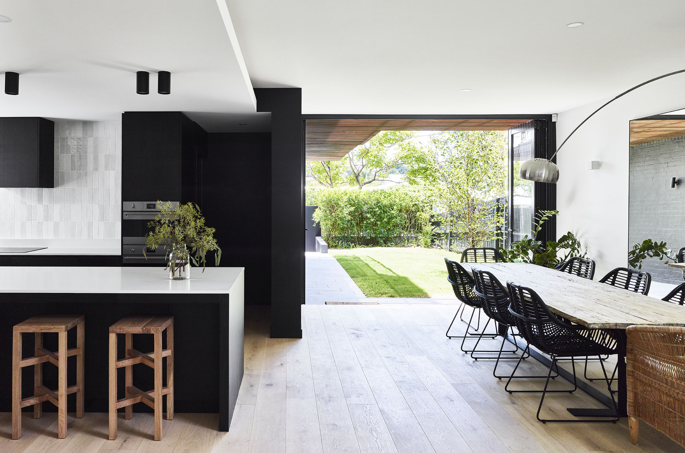 Modern kitchen and dining area opening to a garden, with black cabinetry, timber table, and natural light.