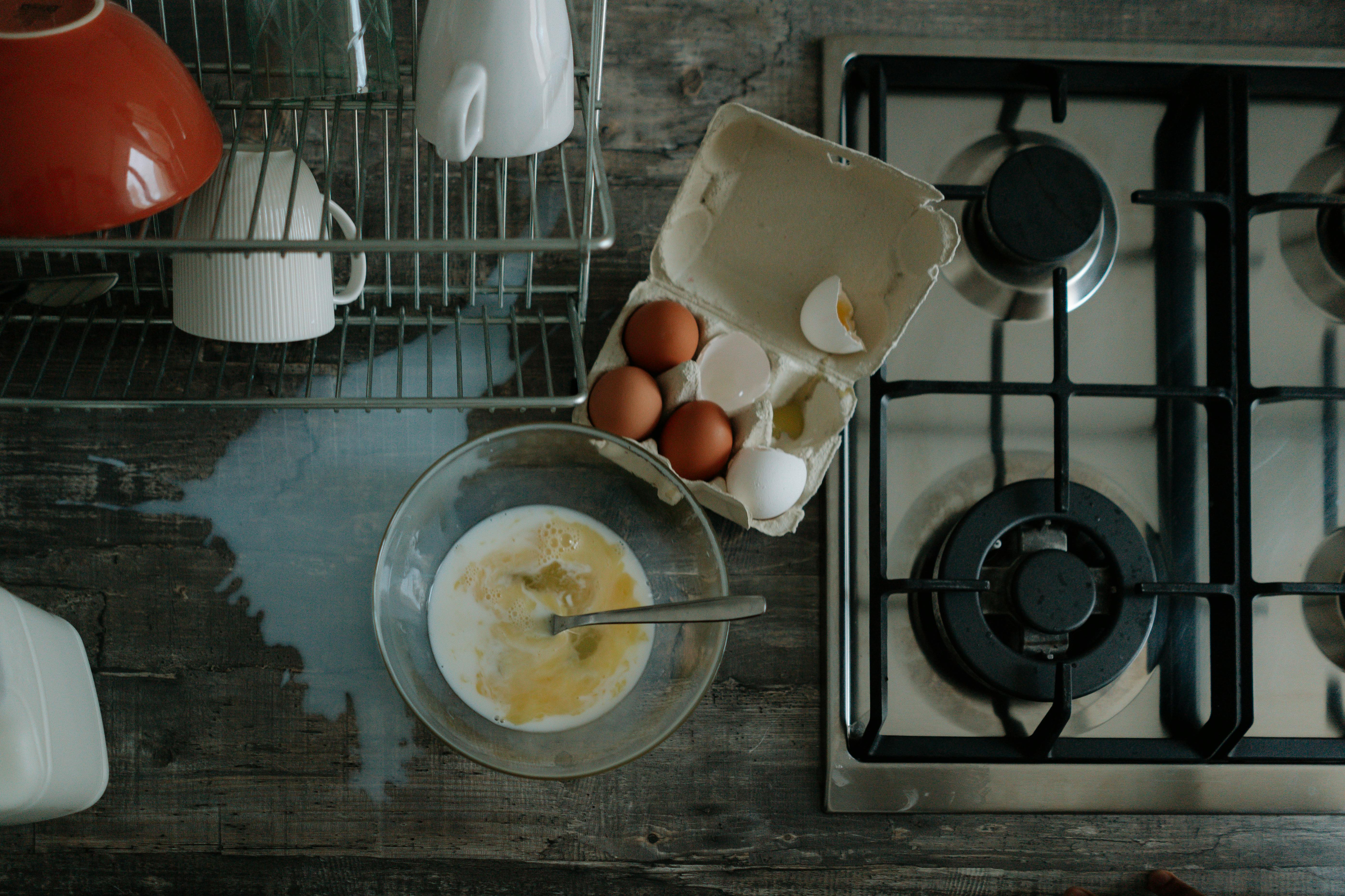 Eggs and milk spilled on a kitchen counter next to a stove and dishrack.