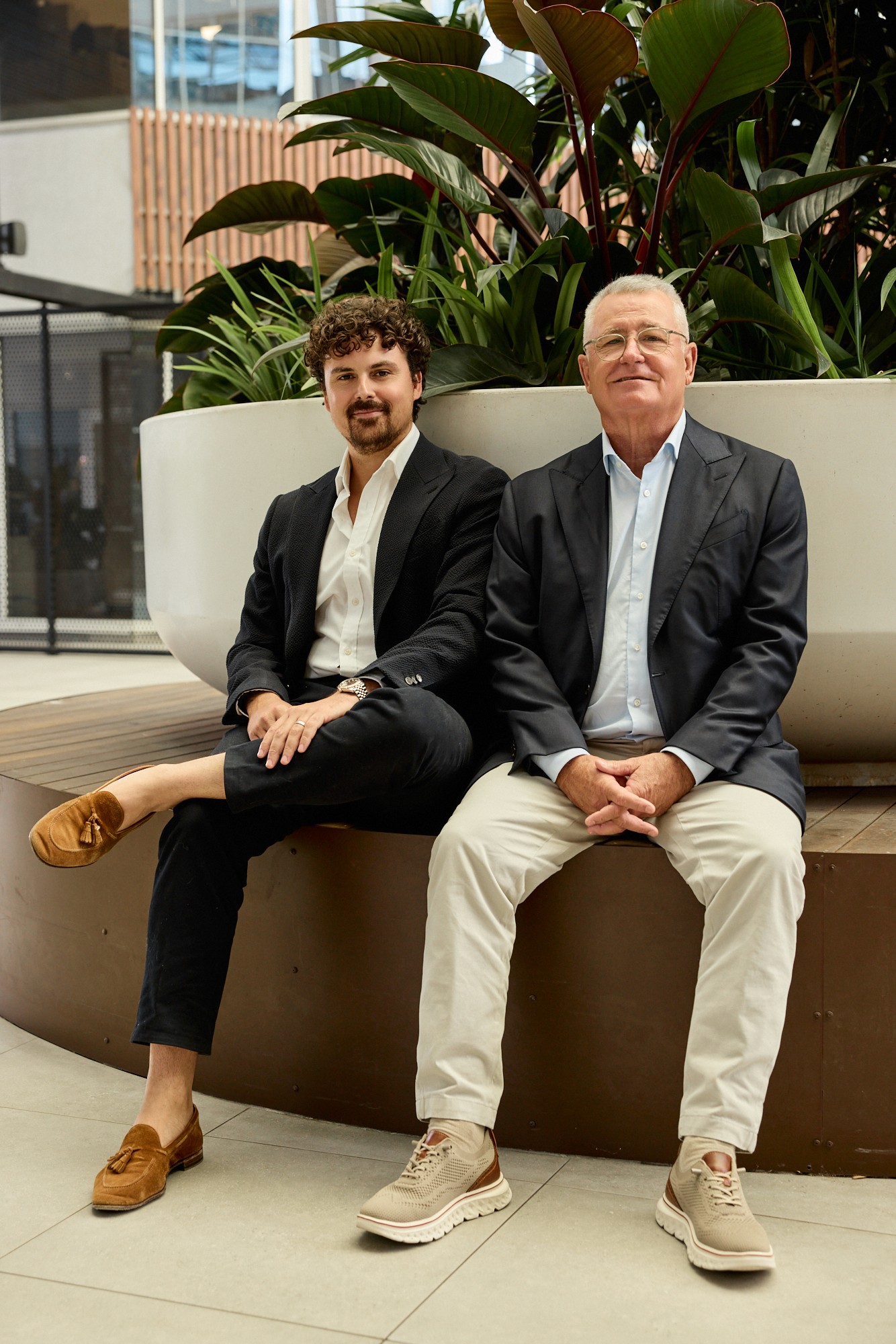 Three people collaborating in a modern office space behind glass with plants and warm lighting.