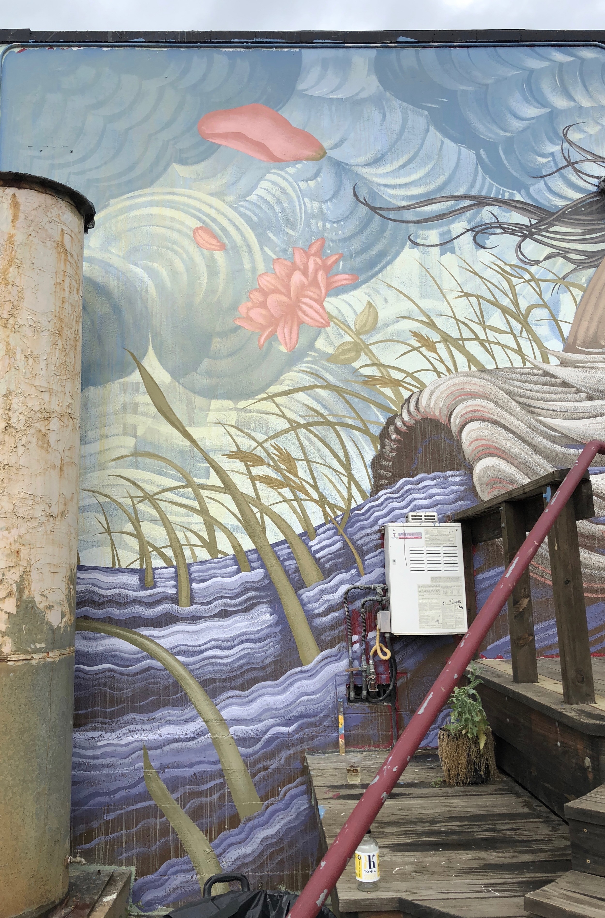 Grasses, pink flowers and pale waves rise up the wall beside a wooden stair.