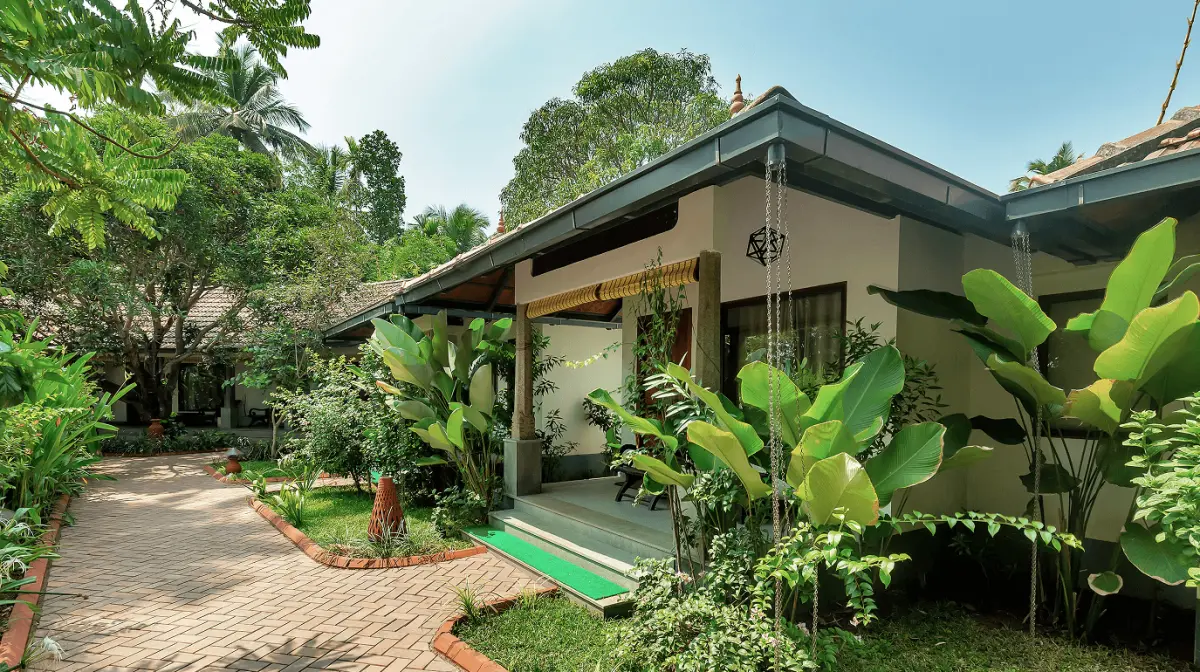 Premier Rooms exterior at Vedic Village Kodungallur with a brick garden path leading through lush tropical foliage to a covered veranda