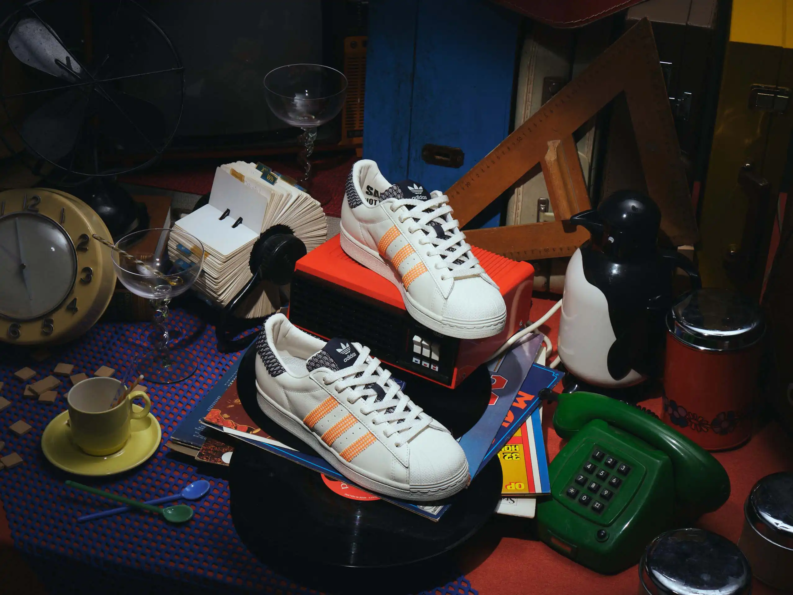 Vintage Adidas sneakers resting on a suitcase beside a felt hat, a chess piece and a miniature camera.