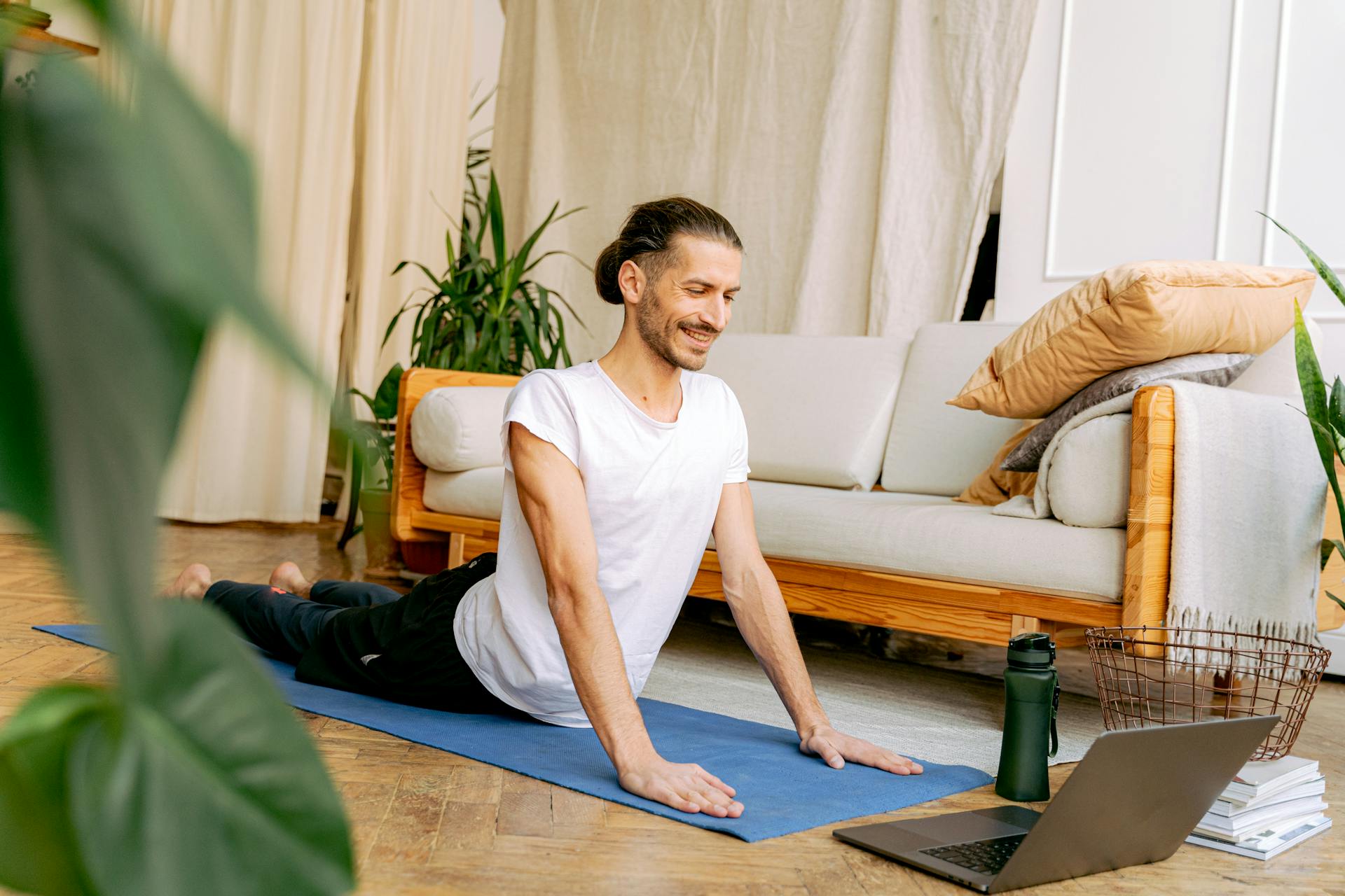 A Man in White Shirt Stretching His Body on the Floor while Looking at the Laptop