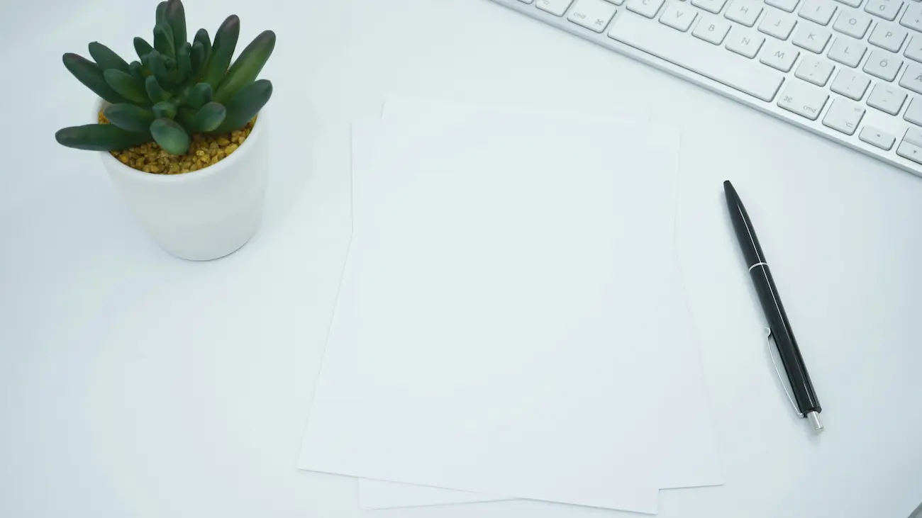 Blank documents with a pen, keyboard and small plant on a clean desk, representing sponsorship documentation, agreements, approvals and organised paperwork for sports clubs.