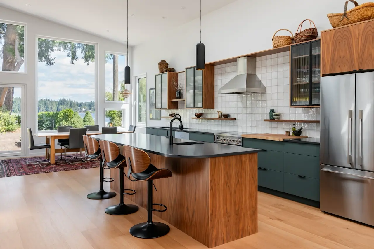 Modern two-story home with large glass windows, warmly lit interiors, and a balcony. Surrounded by trees and a manicured lawn at dusk. Cozy ambiance.