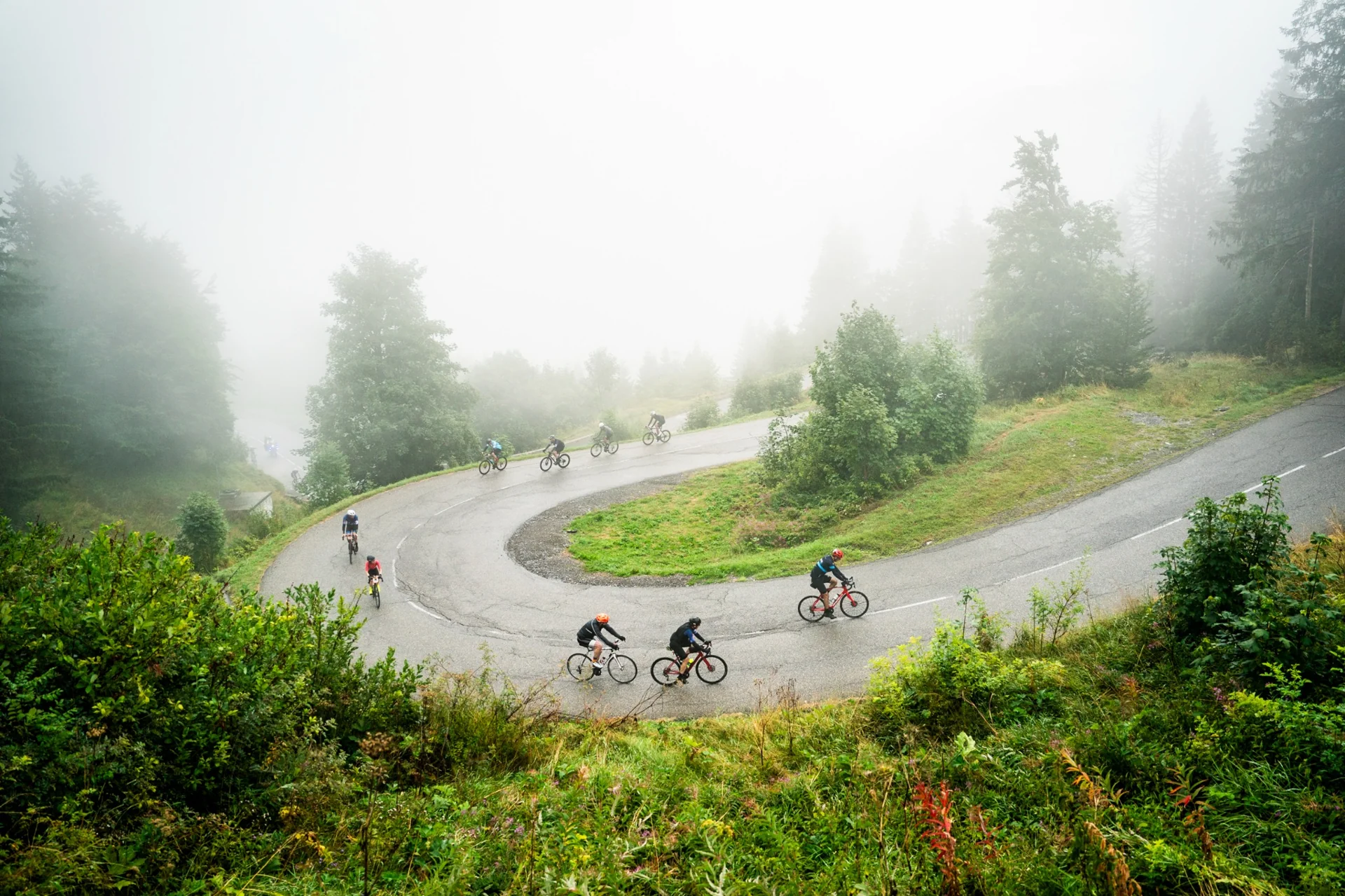 Cyclistes gravissant une route de montagne dans le brouillard lors de la Haute Route Alpes.