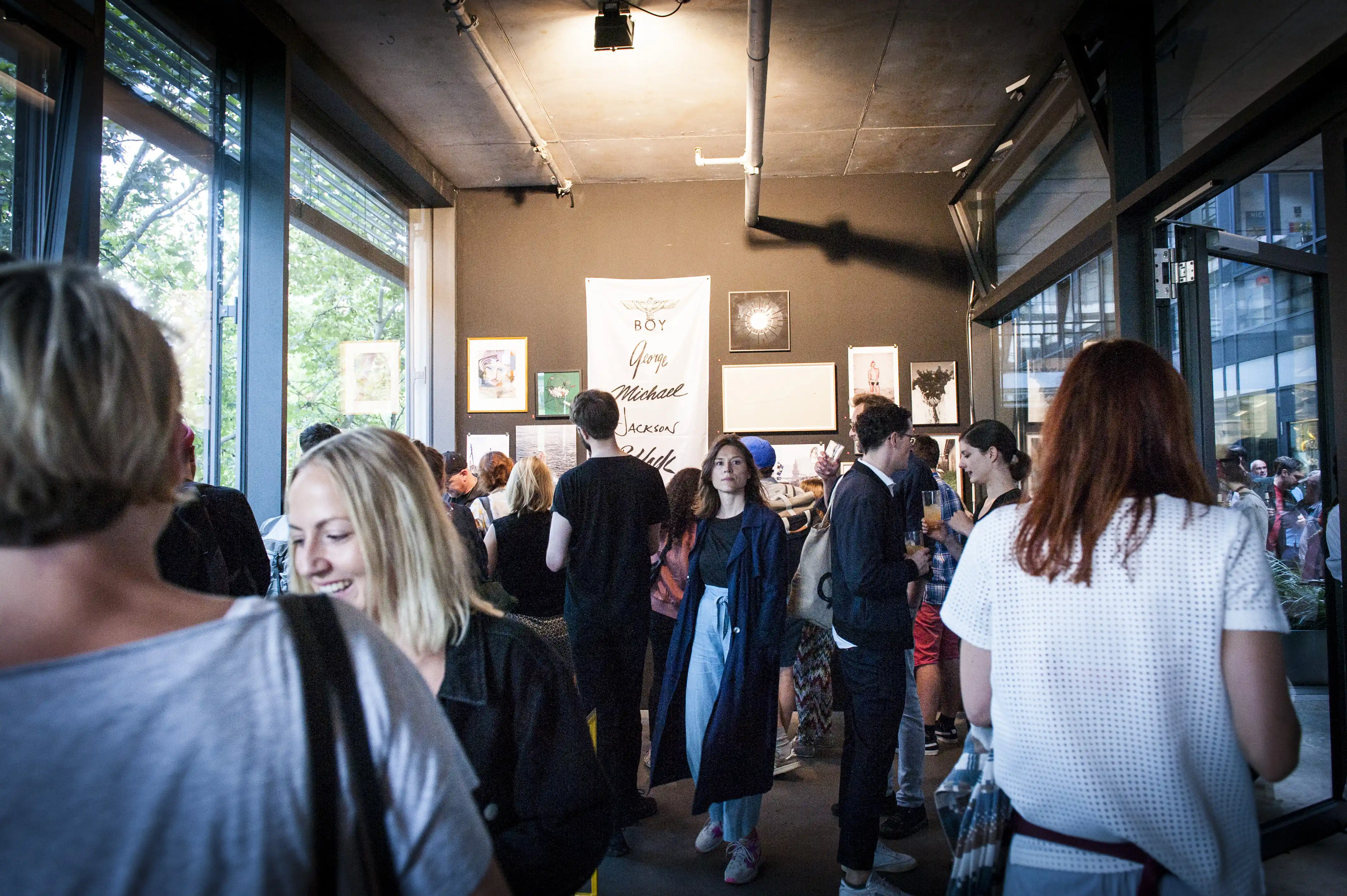 Visitors inside the STUDIOLO gallery during the OHF exhibition with framed artworks and a signed banner on a dark wall.