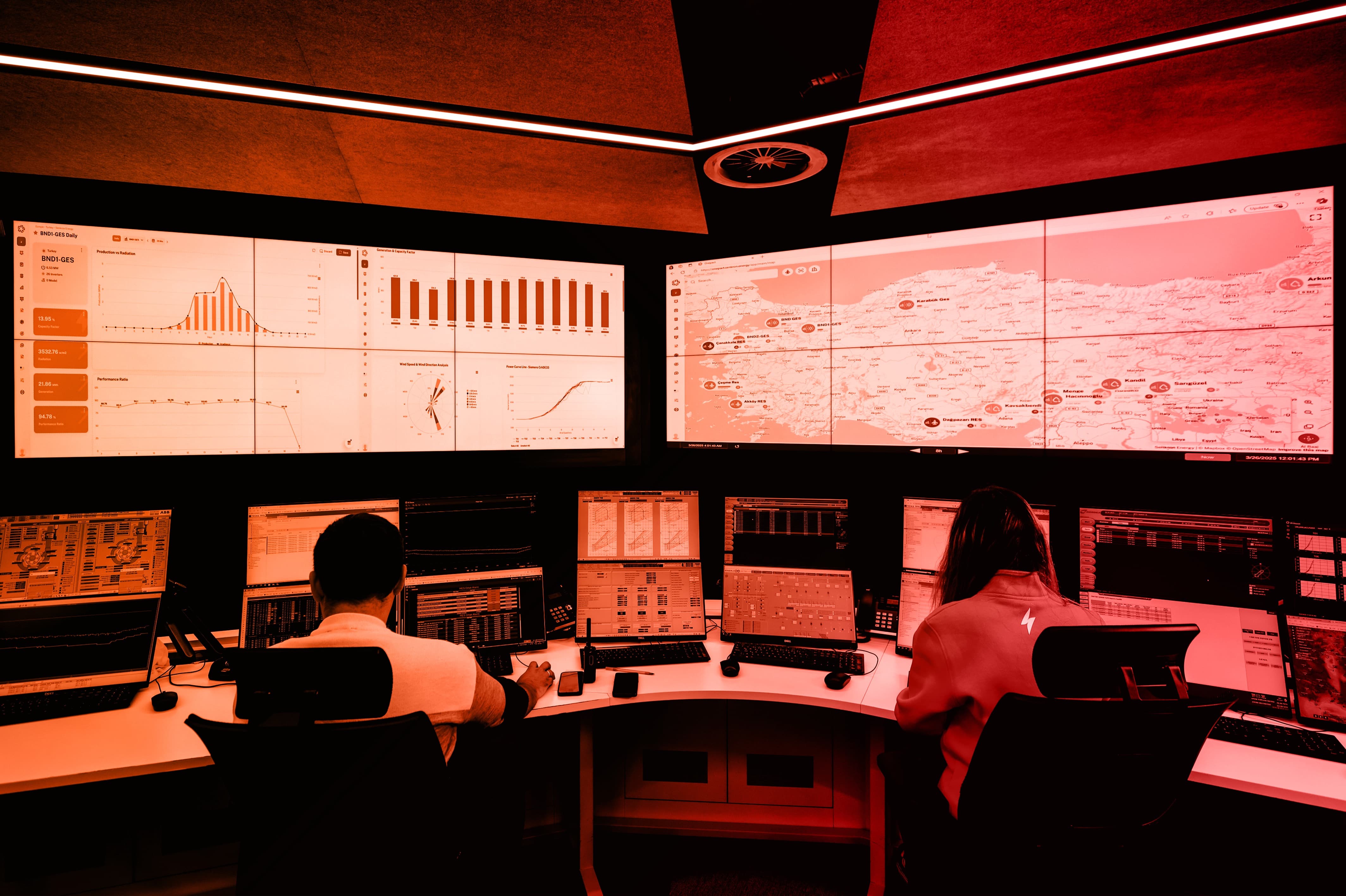 A person sits in front of multiple screens in a dimly lit control room, focused on the displays.