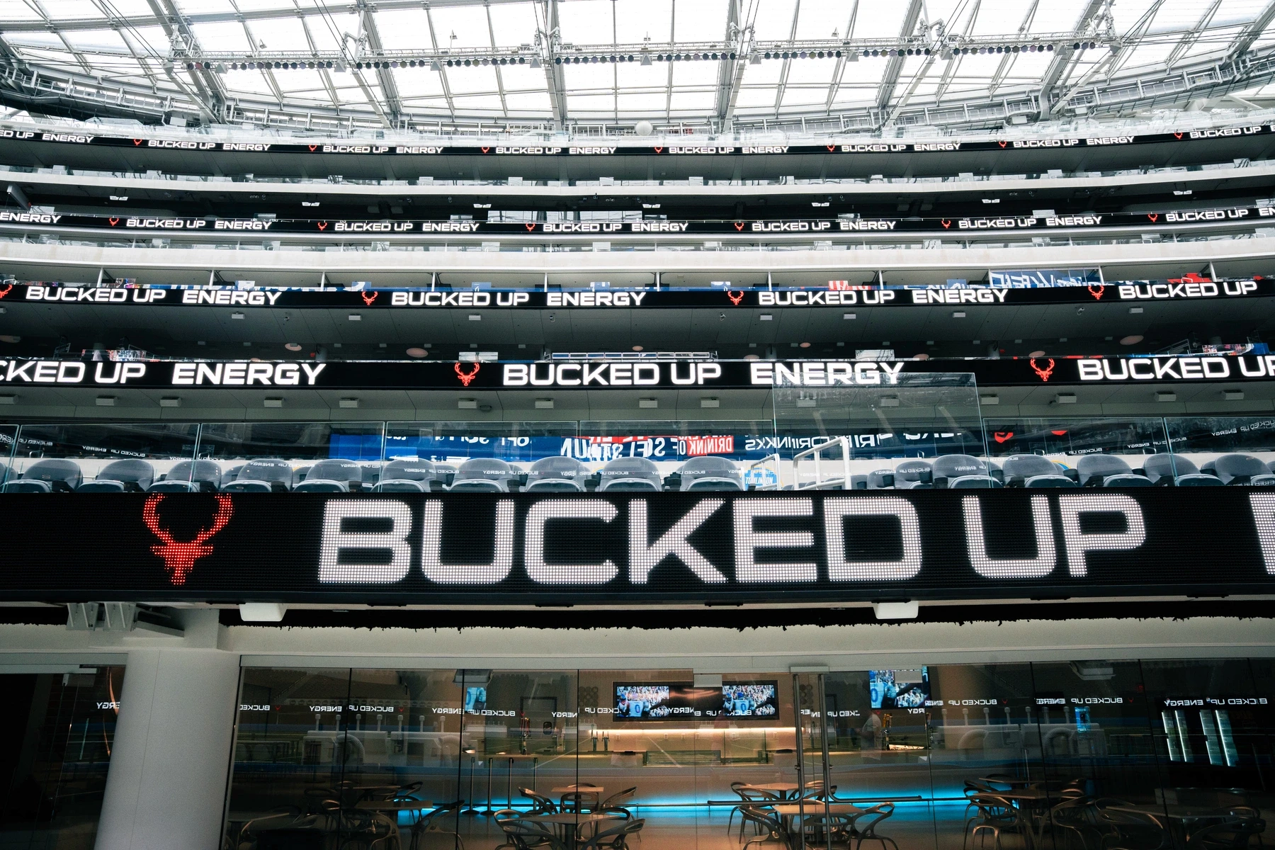 Interior view of SoFi Stadium with multiple LED screens prominently displaying the Bucked Up Energy logo across several levels of seating. The image emphasizes major sponsorship visibility and brand presence in a professional sports venue.