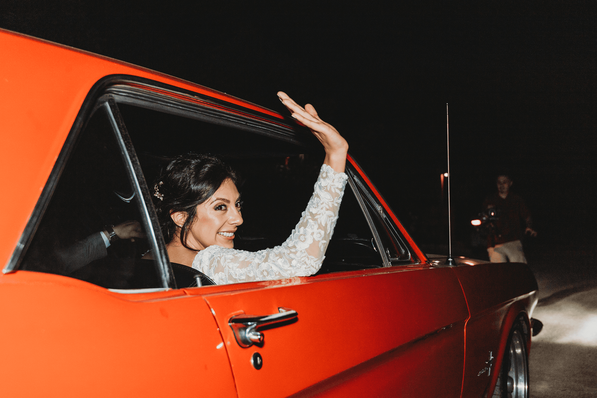 Bride waving goodbye from passenger window as car drives away at night
