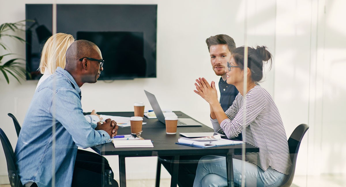 Small team collaborating around a conference table with laptops and coffee in a modern meeting room