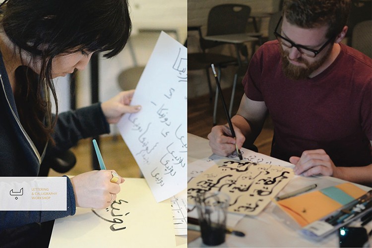 The image is a diptych showing a woman and a man engaged in calligraphy. The woman, on the left, is seated at a table with a light-colored surface, holding a white sheet of paper with black calligraphy and holding a pen in her right hand. She is wearing a dark-colored jacket or cardigan. The man, on the right, is seated at a table with a light-colored surface, wearing a maroon t-shirt and glasses. He is holding a brush in his right hand and appears to be writing on a white sheet of paper with a brush in his left hand. The table contains various art supplies, including a cup, a pen holder, and a notebook or pad of paper. The background is blurred but shows other furniture, suggesting a workshop or studio setting.