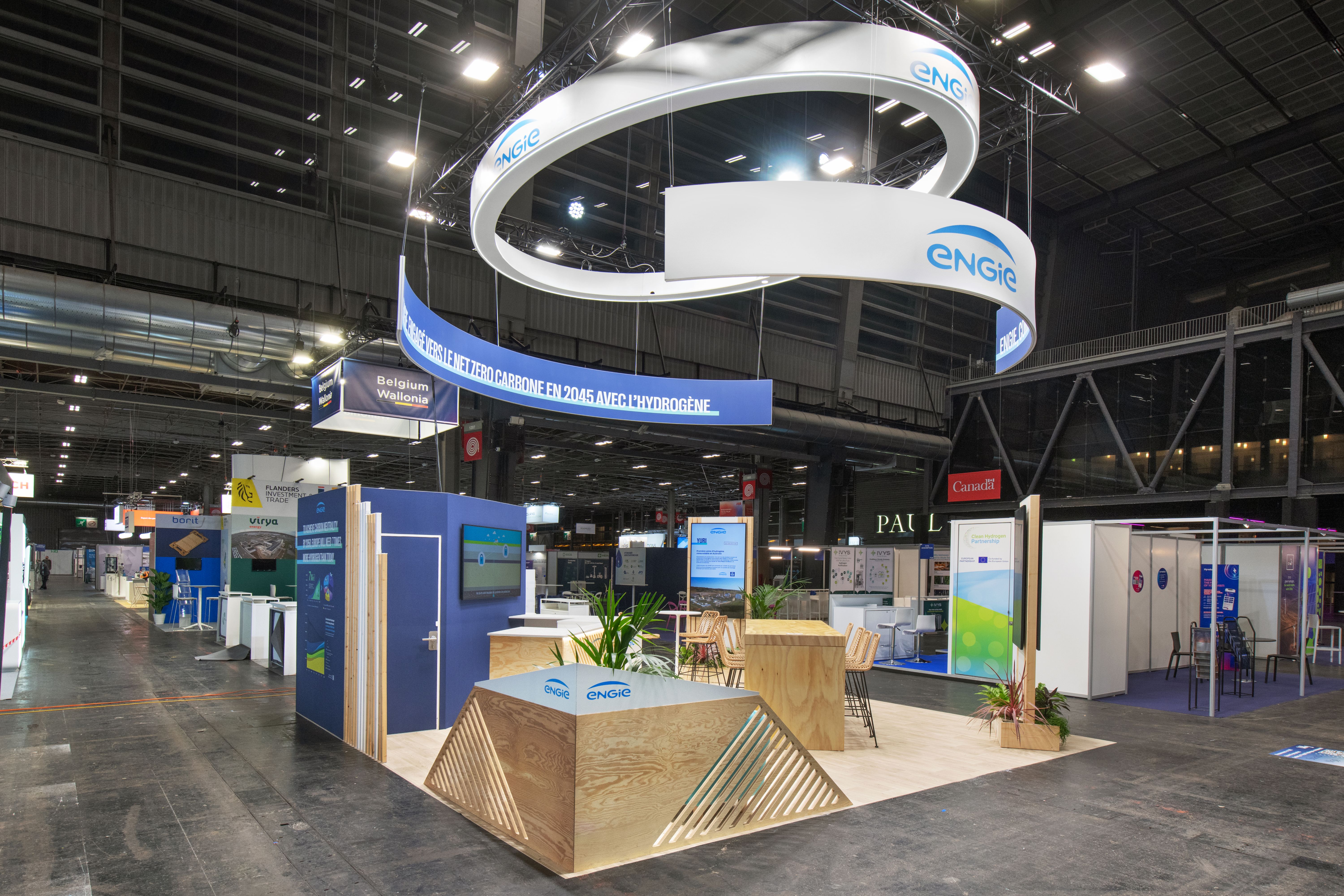 Stand ENGIE salon Hyvolution Paris 2026 réalisé par Expace – vue intérieure avec couronne lumineuse suspendue bleue et blanche, espace végétalisé bois clair et zone information hydrogène