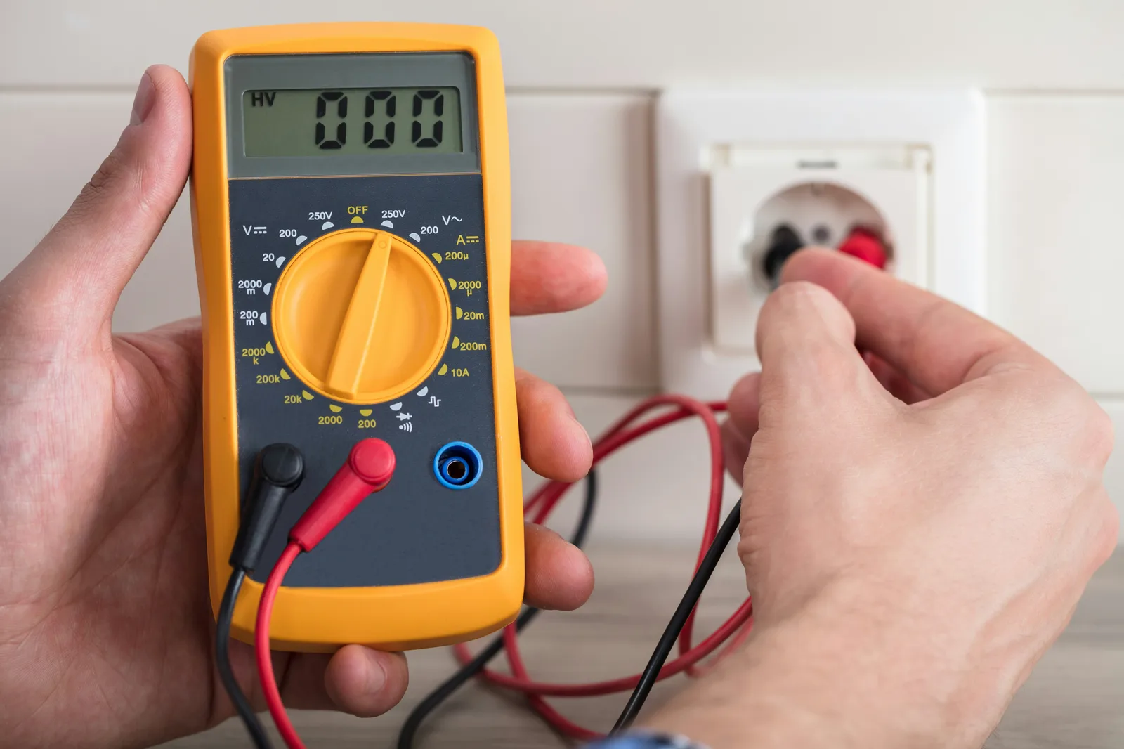Electrician holding digital multimeter and testing wall outlet voltage
