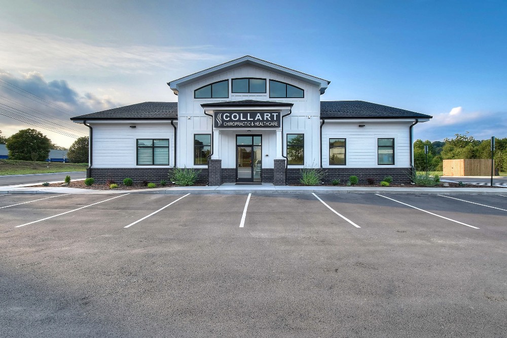 A modern building with a symmetrical facade, featuring a peaked roof and a parking lot in front under a clear sky.