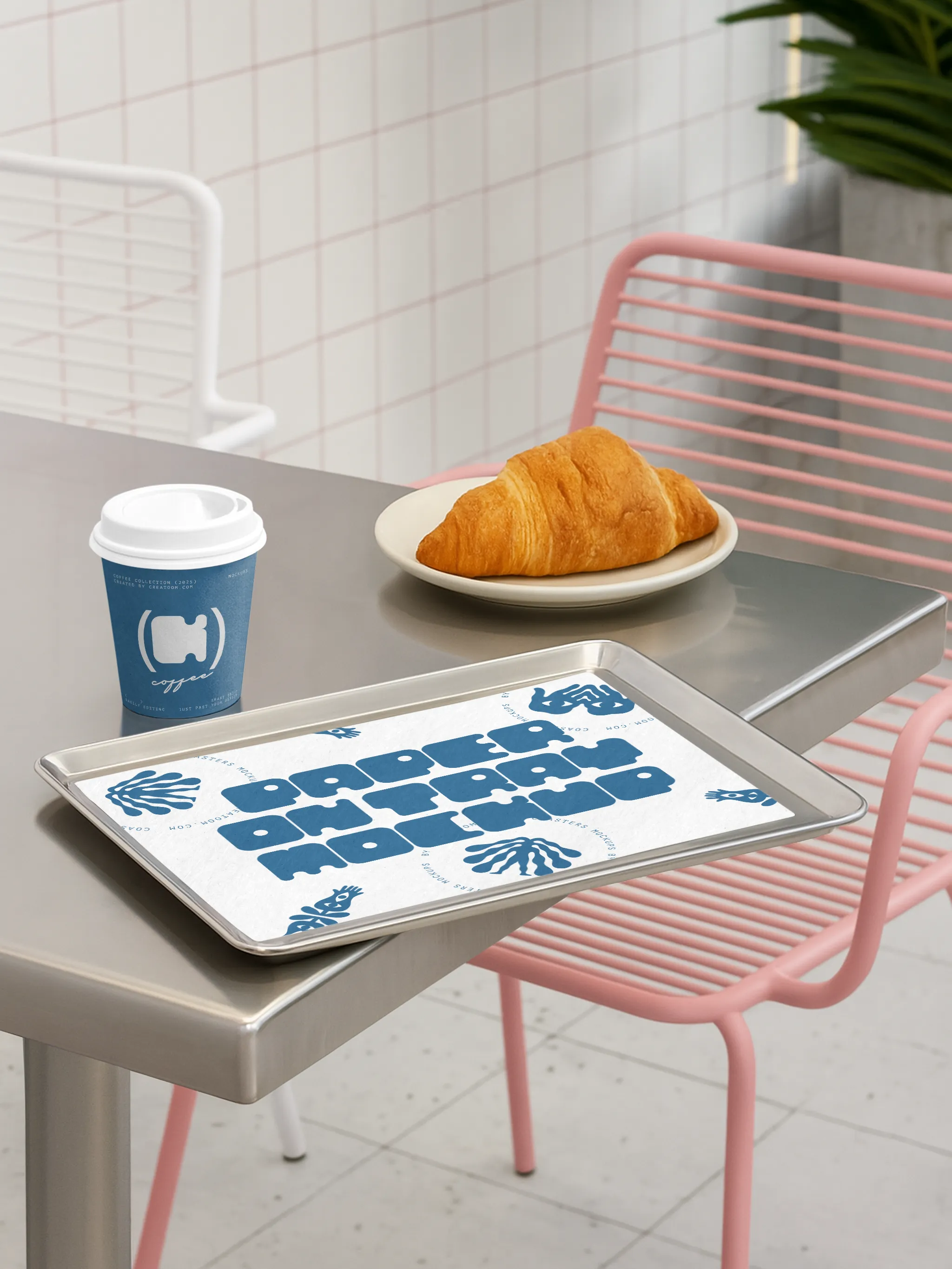 Coffee cup with branded sleeve on metal counter beside a croissant and branded tray liner