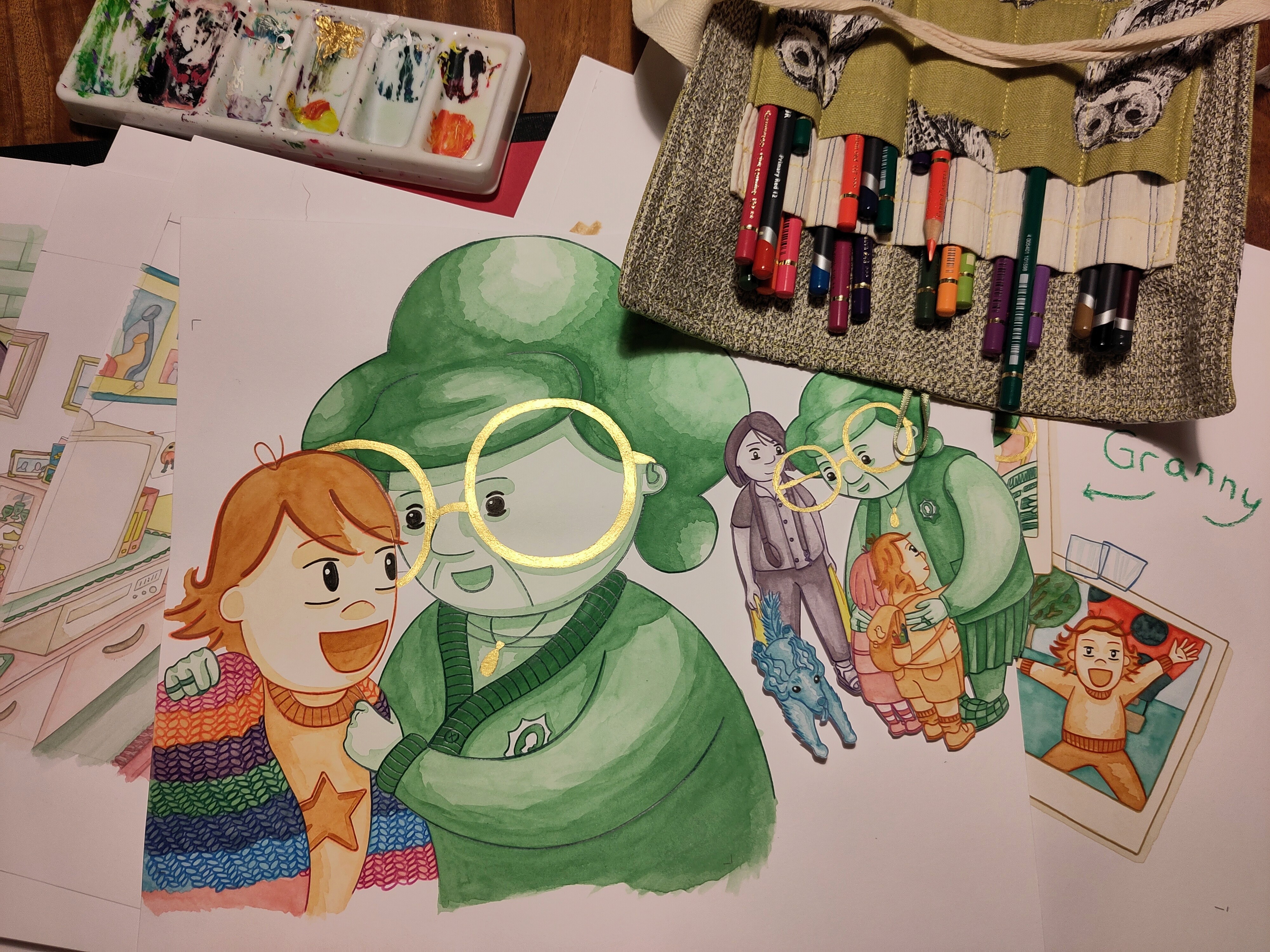 A photo of a few illustrations from the book. The most prominent illustration is of Granny and her granddaughter the illustration that is used on the cover of the book. It has been fully painted, pencil crayon lined and Granny's glasses have been painted gold. The role of pencils is open showing all the pencil crayons that were used to line the pictures.