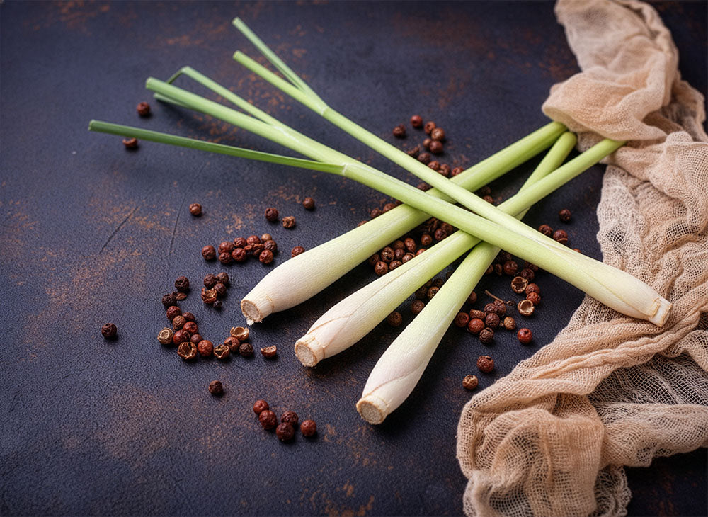 Lemongrass and red peppercorns on a dark surface with a beige cloth.
