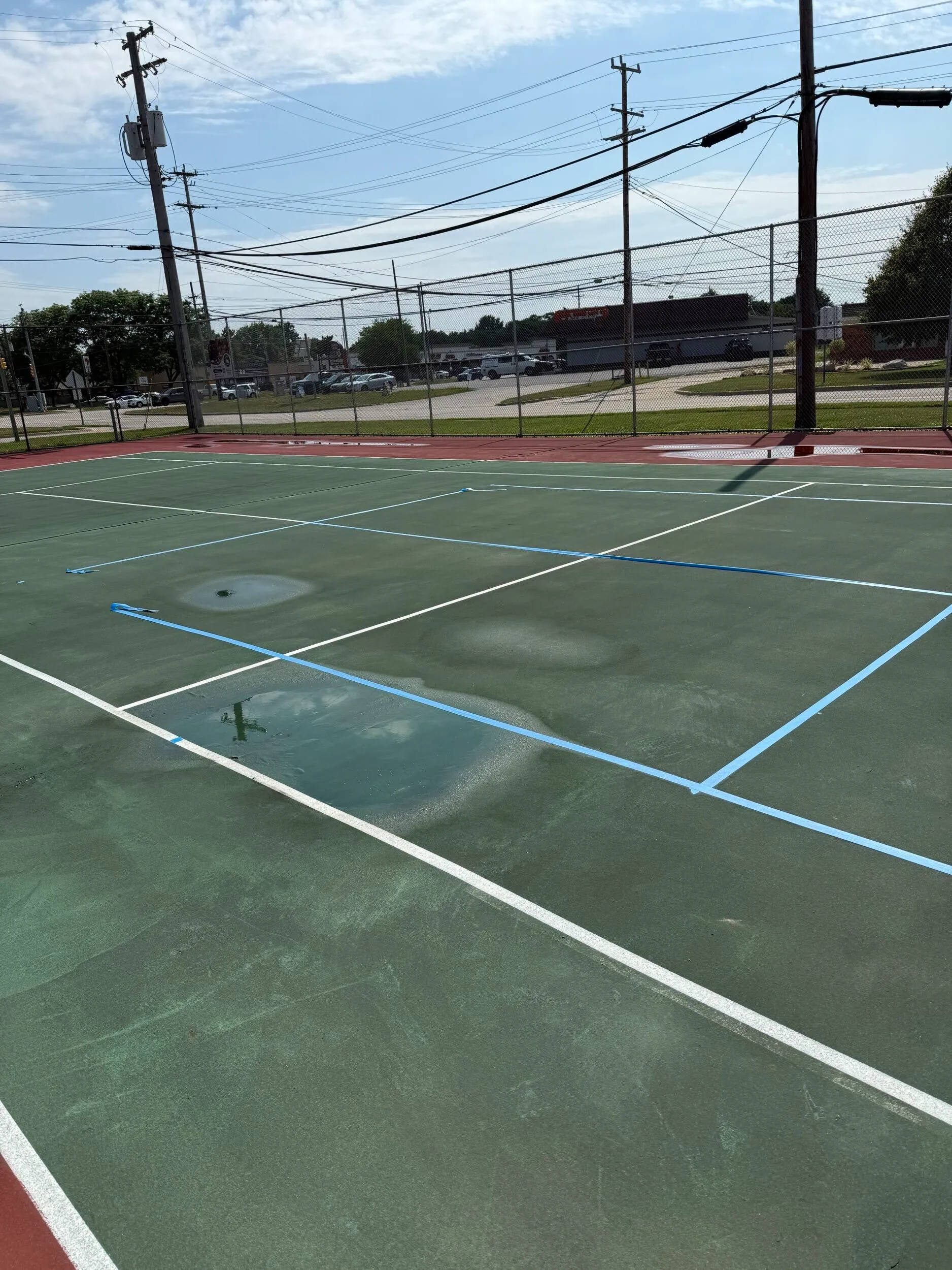 Worn tennis courts with standing water before pickleball conversion at Clintondale Community Schools