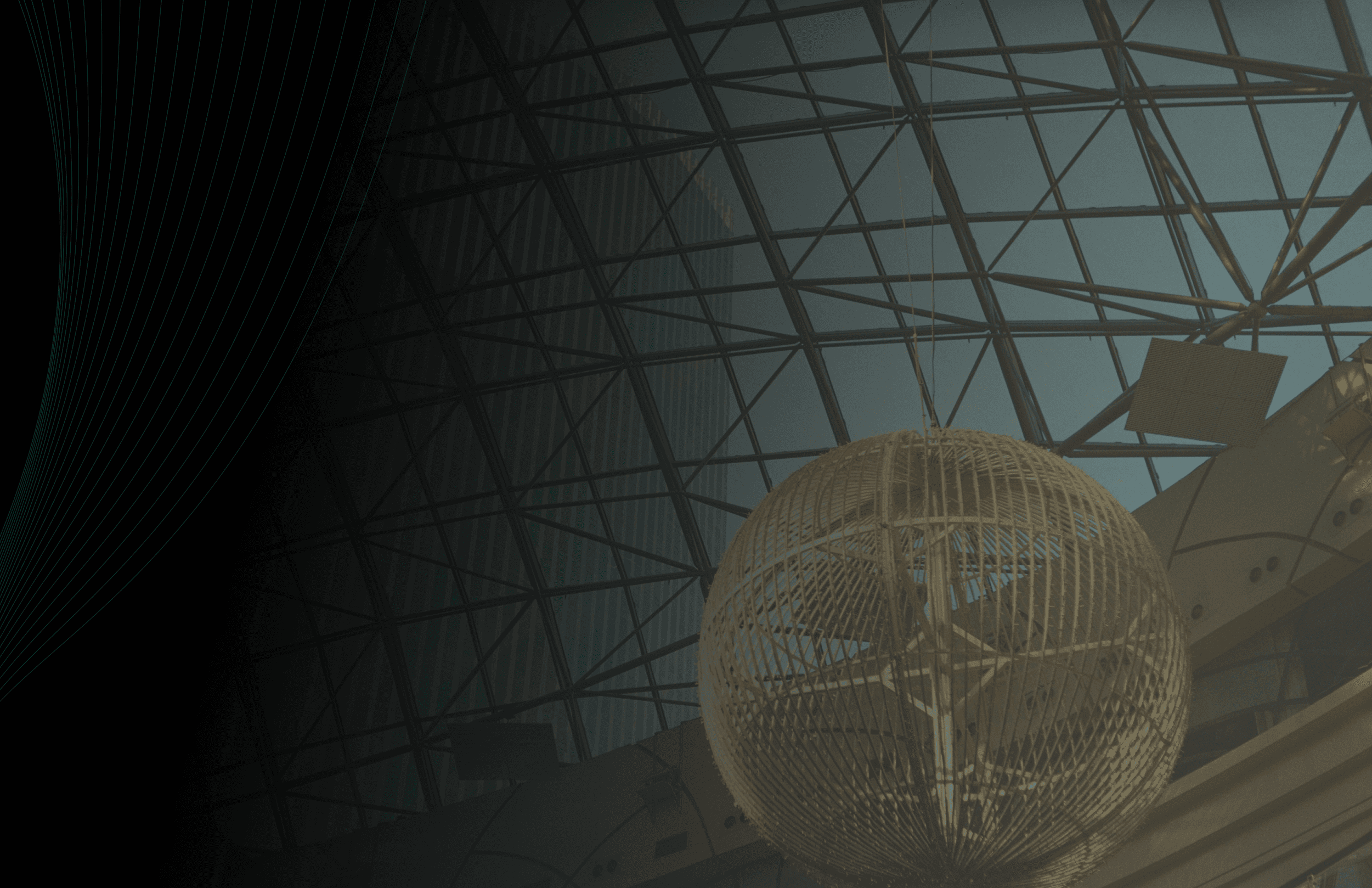 Modern glass atrium architecture featuring a large spherical light installation under a steel grid roof.