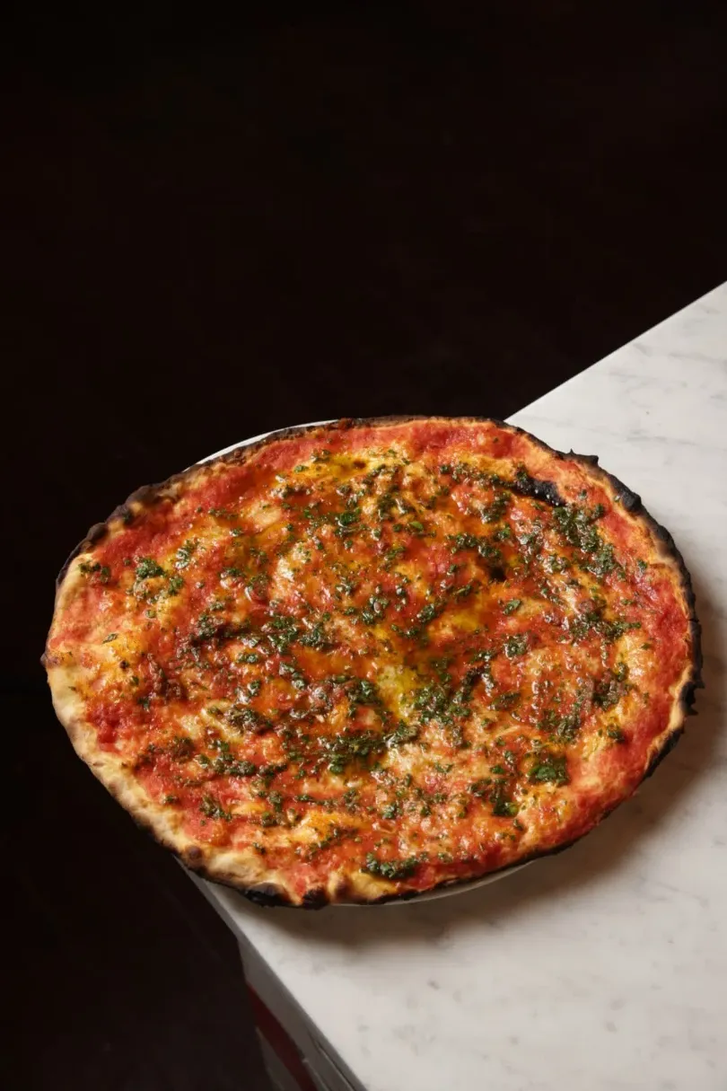 A freshly baked pizza topped with various vegetables and melted cheese, placed on a white marble surface.