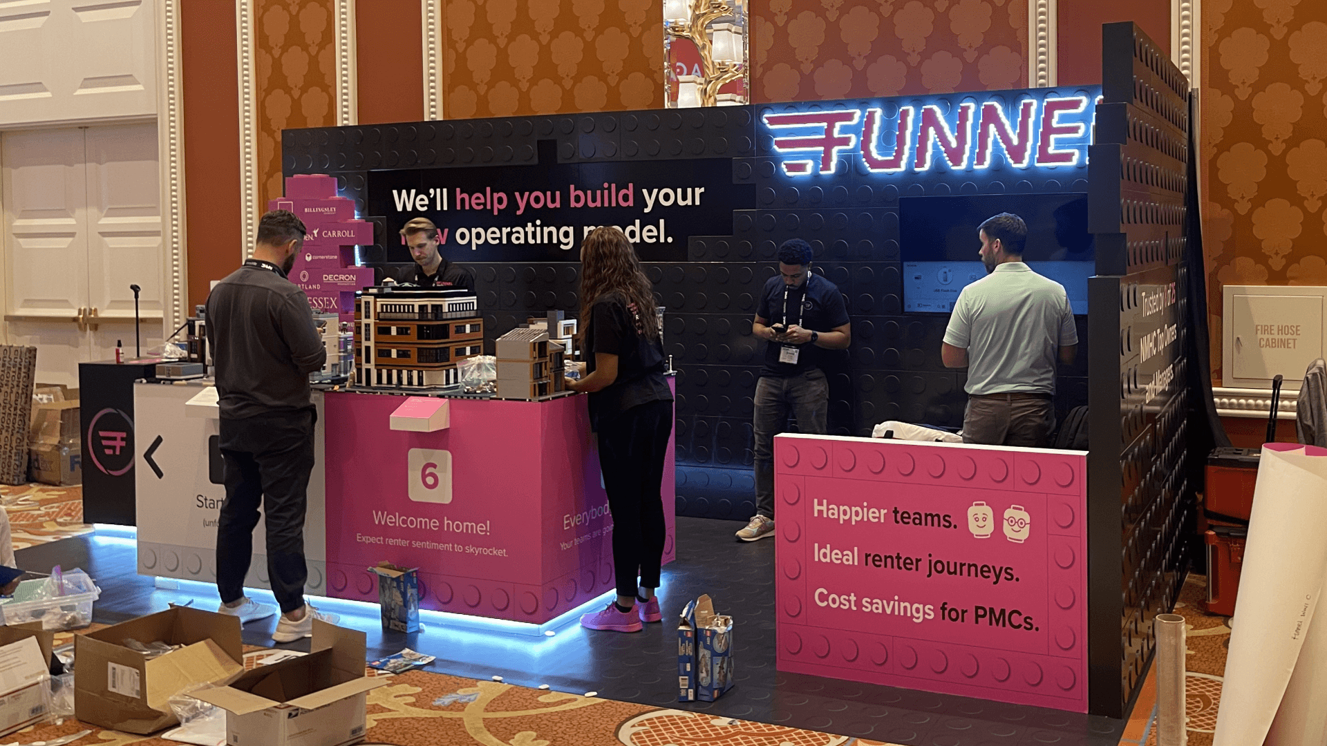 Funnel OPTECH 2023 10x20 small inline booth with black branded backwall, illuminated logo, pink counters, screen display, and property model presentation area.