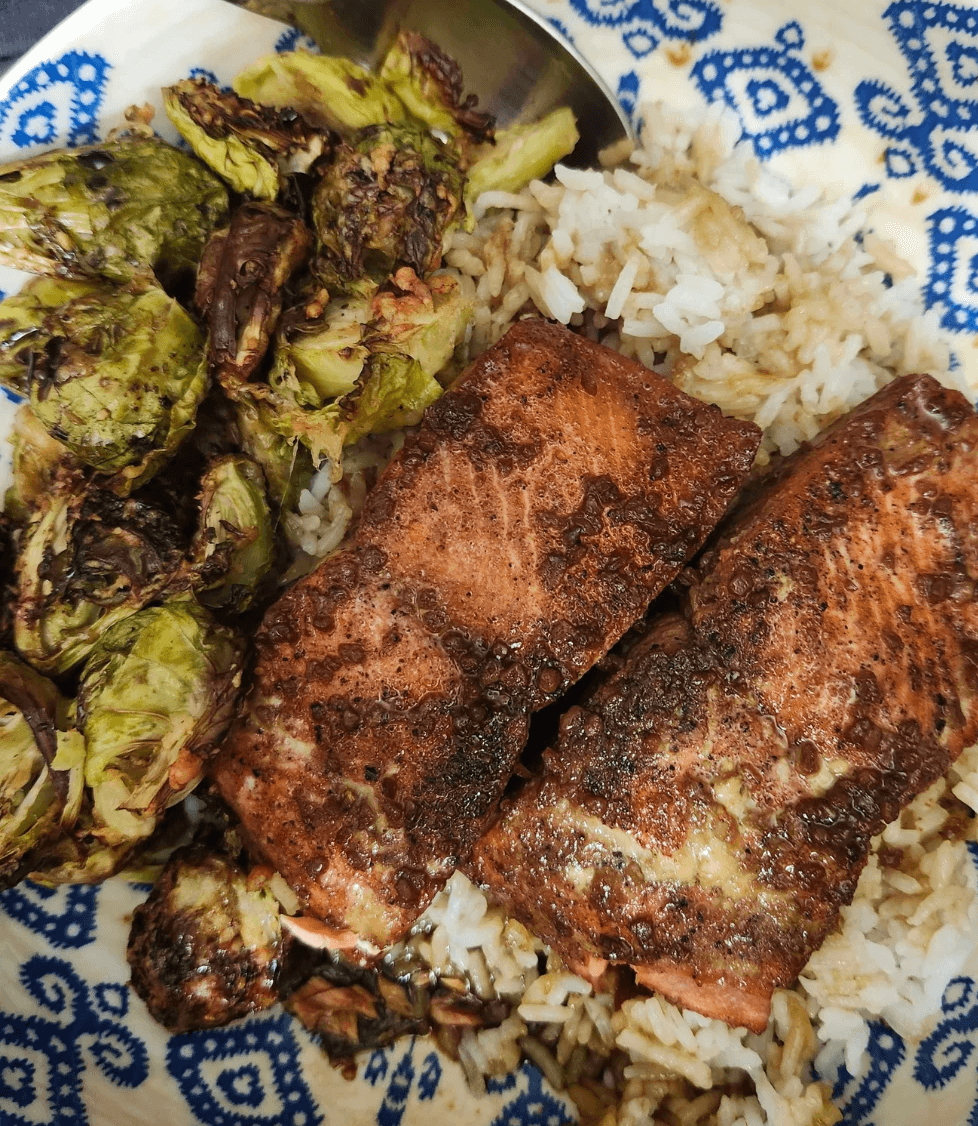 Honey-glazed salmon served with roasted Brussels sprouts and rice on a patterned plate.