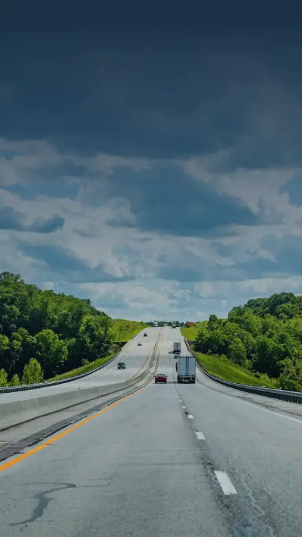 Open highway surrounded by green trees under a partly cloudy sky, representing GIA Group, LLC’s commitment to guiding truckers with clear answers and reliable insurance support.