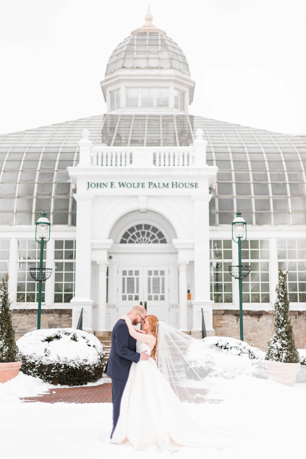Bride and groom portrait in front of greenhouse during the winter with snow.