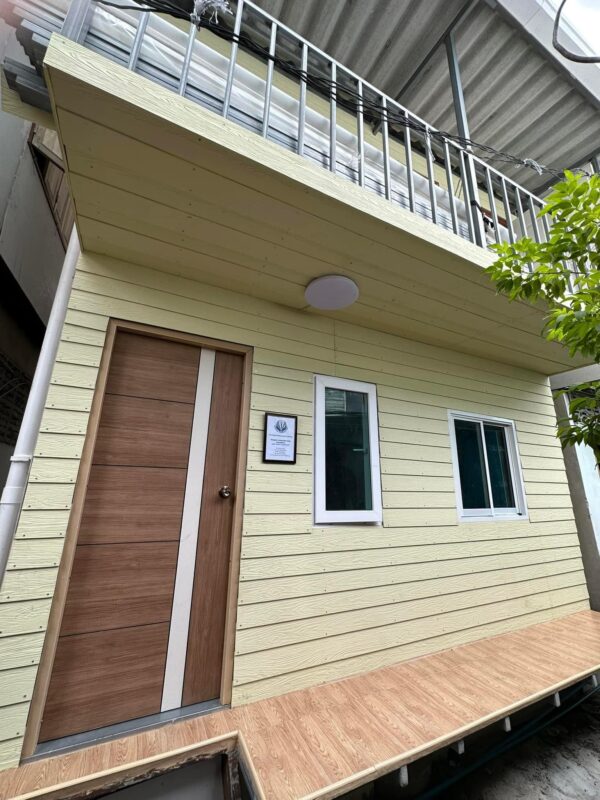 man in blue t-shirt and white floral skirt holding black smartphone while sitting on sidewalk