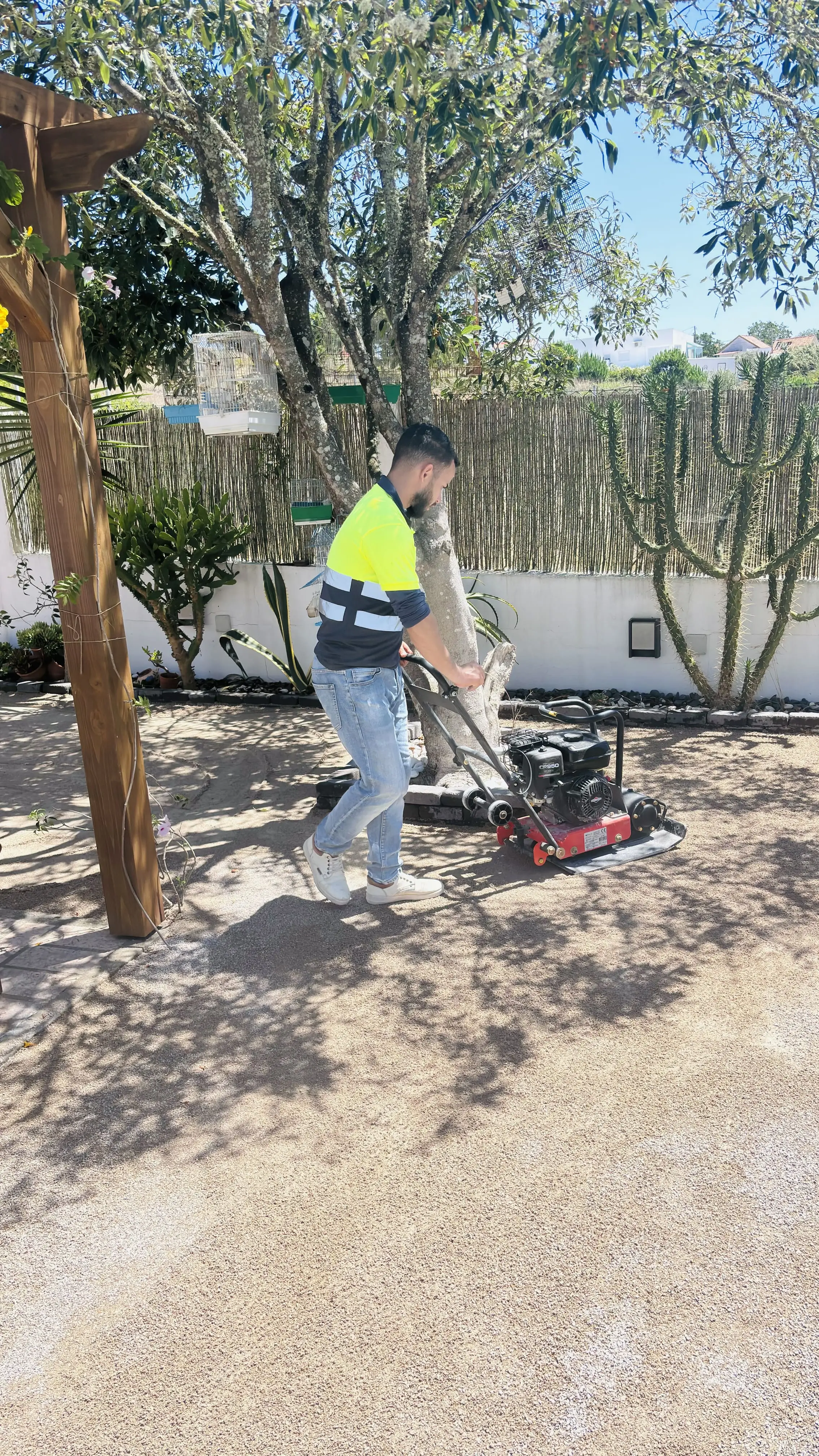 Profissional realizando manutenção regular de jardim residencial, incluindo corte de relva e cuidados com plantas ornamentais