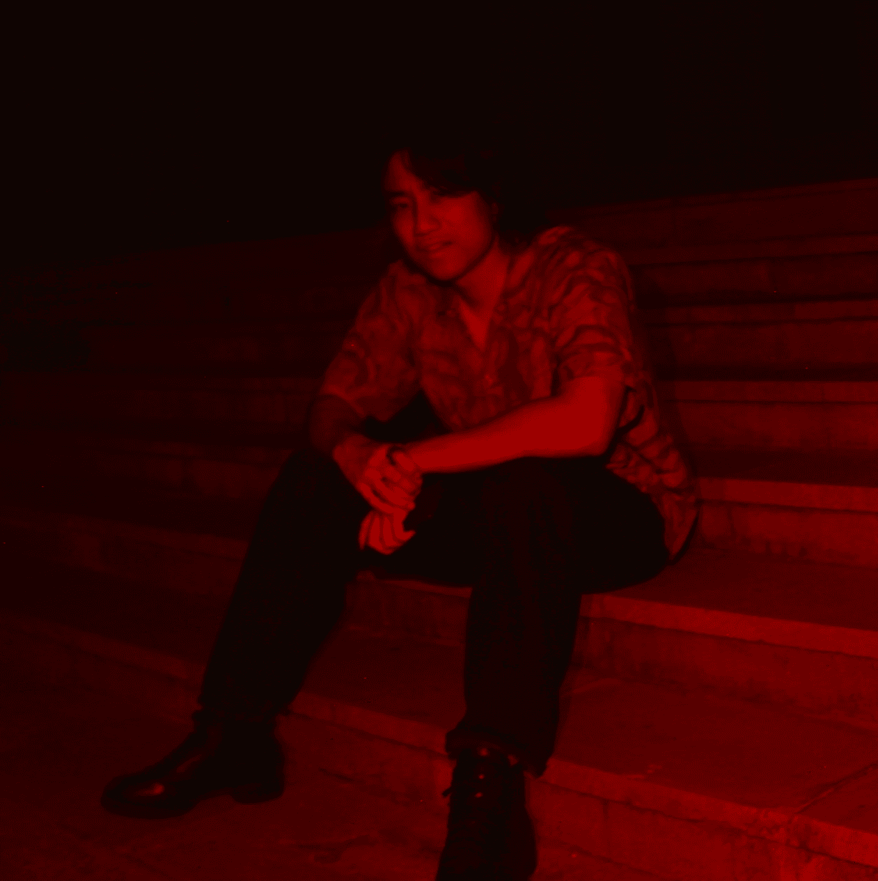 black and red image of man looking at camera while sitting on steps