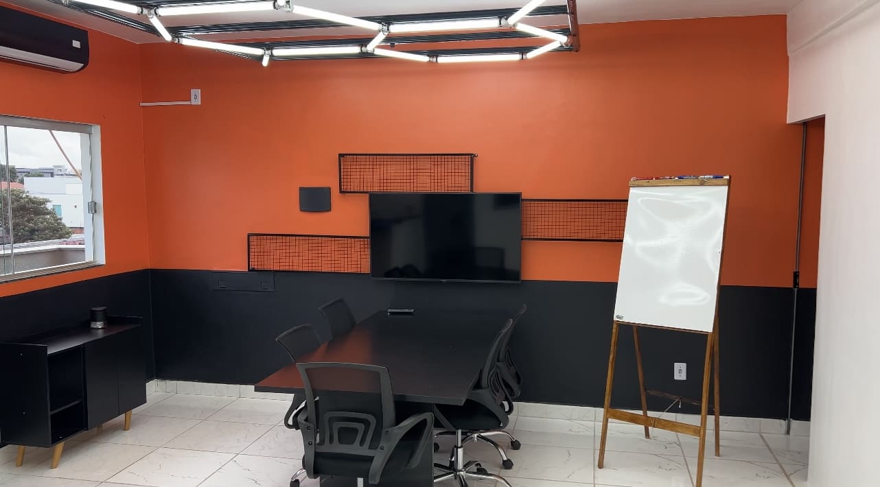 Sala de reuniões moderna com mesa, cadeiras ergonômicas, TV e quadro branco, em ambiente corporativo com design contemporâneo e iluminação em LED.