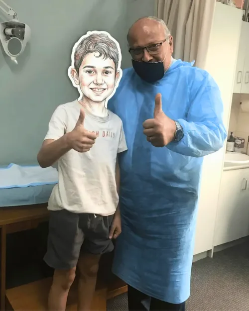 Dr. Ashraf Saddik giving a thumbs up beside a smiling school-age boy in a medical examination room.