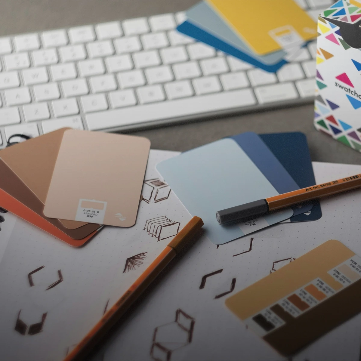 A desktop scattered with tools normally used on design or branding projects such as paint swatches, logo sketches, pencils, and a keyboard for digital design
