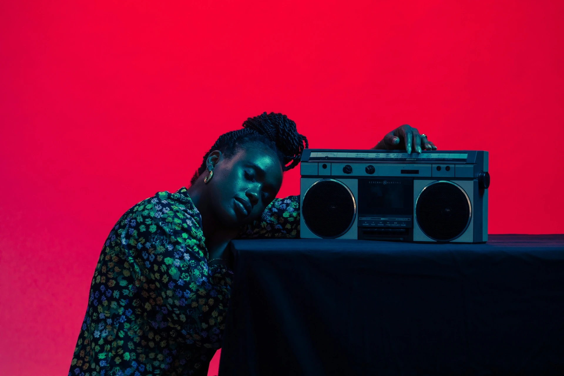 Person lehnt an einem Kassettenrekorder vor rotem Hintergrund – visuelle Metapher für Zuhören, Wahrnehmung und kulturelles Verständnis.