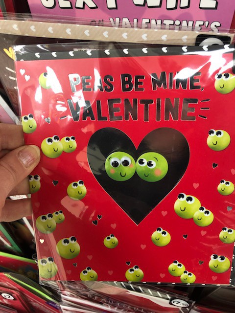A humorous red Valentine's Day card reading "Peas Be Mine, Valentine" decorated with cartoon smiling pea characters.
