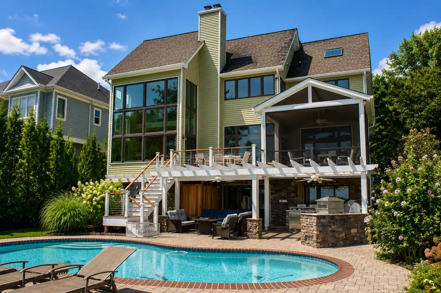 Waterfront home after renovation featuring a multi-level deck, screened porch, covered patio, outdoor kitchen, stonework, and poolside entertaining area.