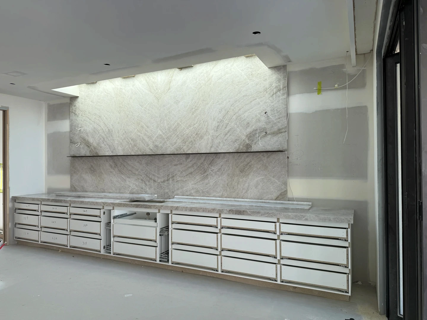 Very large marble splashback panels installed floor to ceiling, showcasing bold natural stone veining above a run of commercial cabinetry for a striking oversized feature.