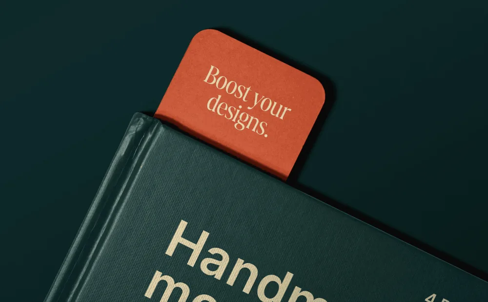 Close-up of a green hardcover book with a textured surface, featuring a red bookmark partially inserted at the top. The bookmark contrasts with the book, set against a dark green background.