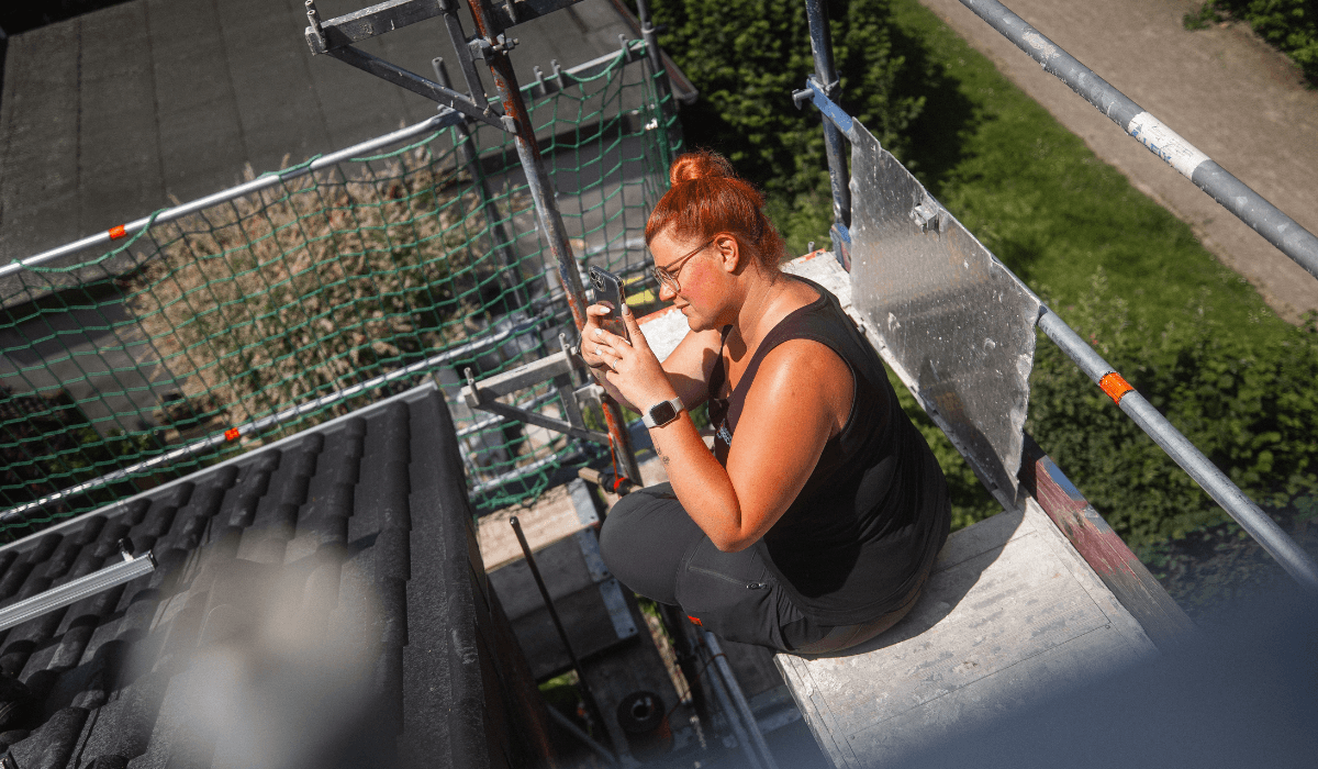 Mitarbeiterin sitzt auf einem Gerüst und fotografiert
