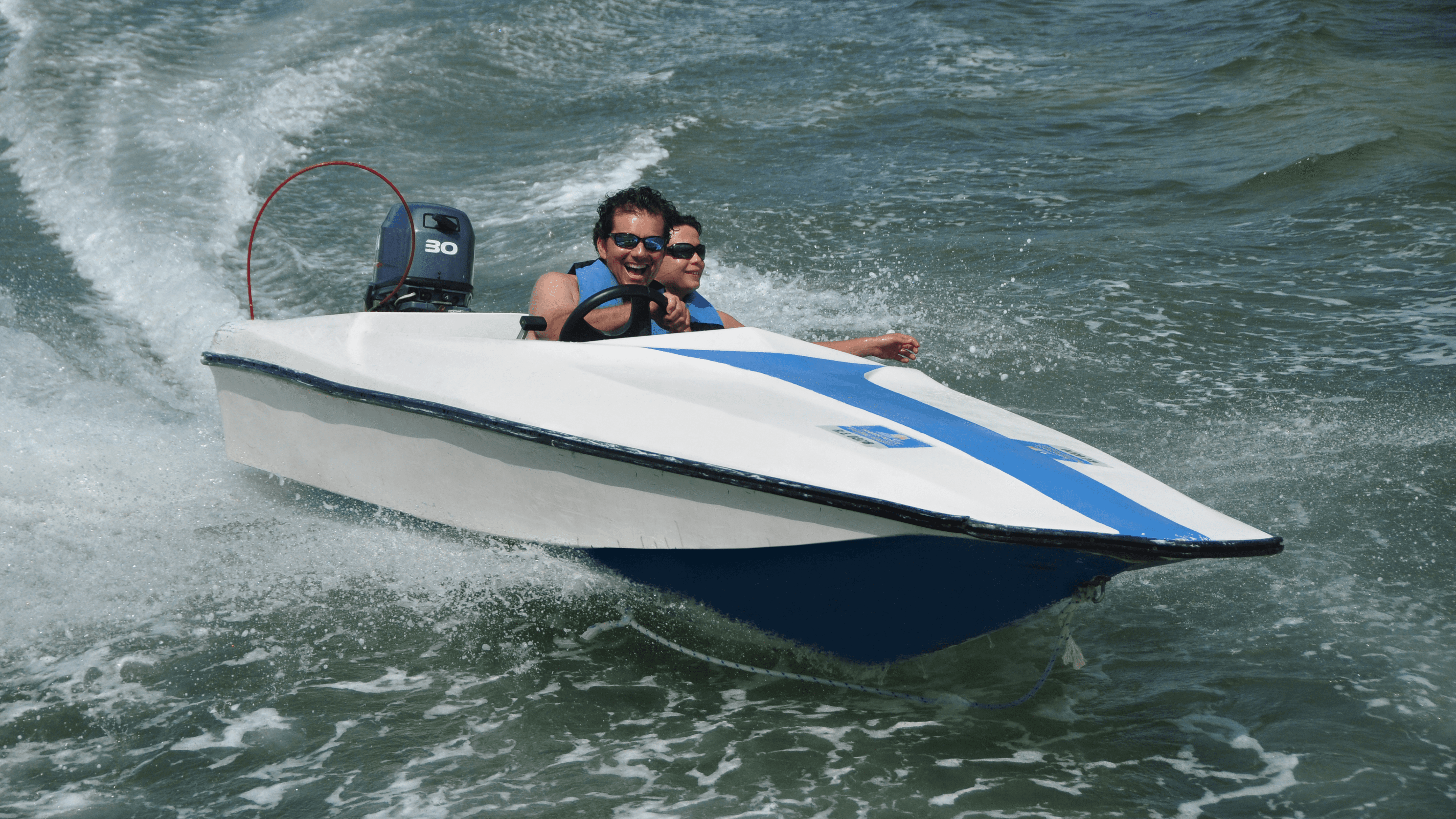 Two men driving a small white and blue speedboat through choppy water